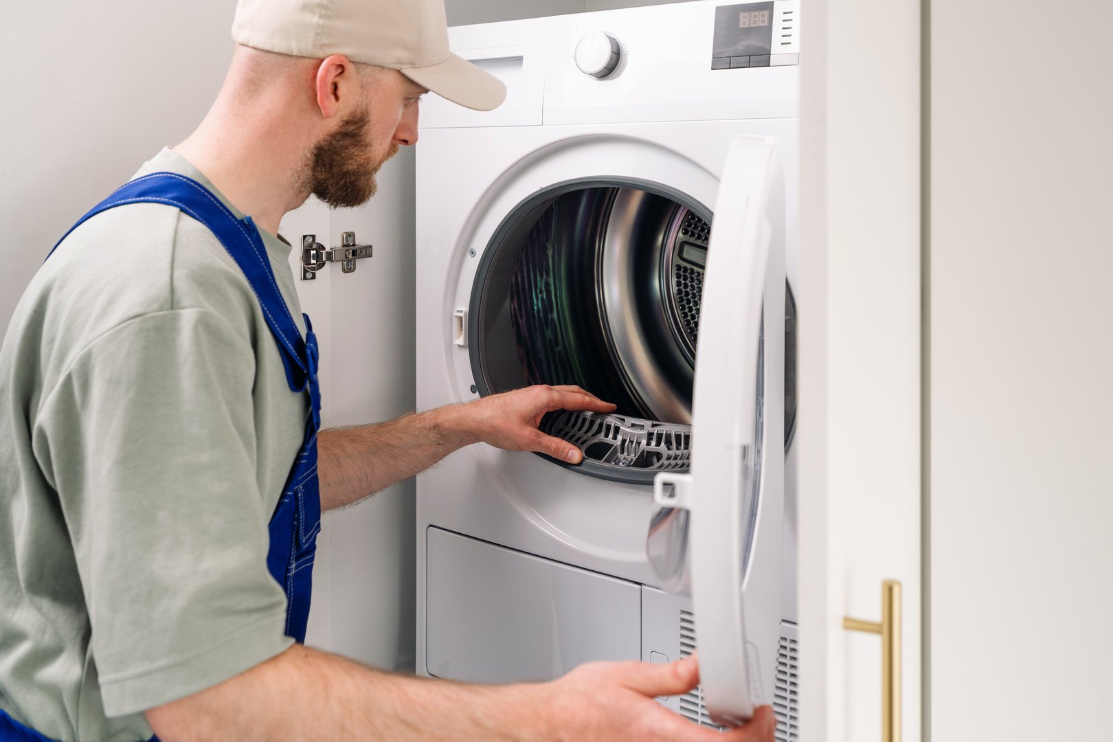 Technician performs maintenance on an automatic washing machine, inspecting rubber and drum with internal components in a laundry room, focused on ensuring optimal performance and reliability.