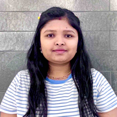A woman with long black hair wearing a patterned sweater smiles at the camera against a plain background.
