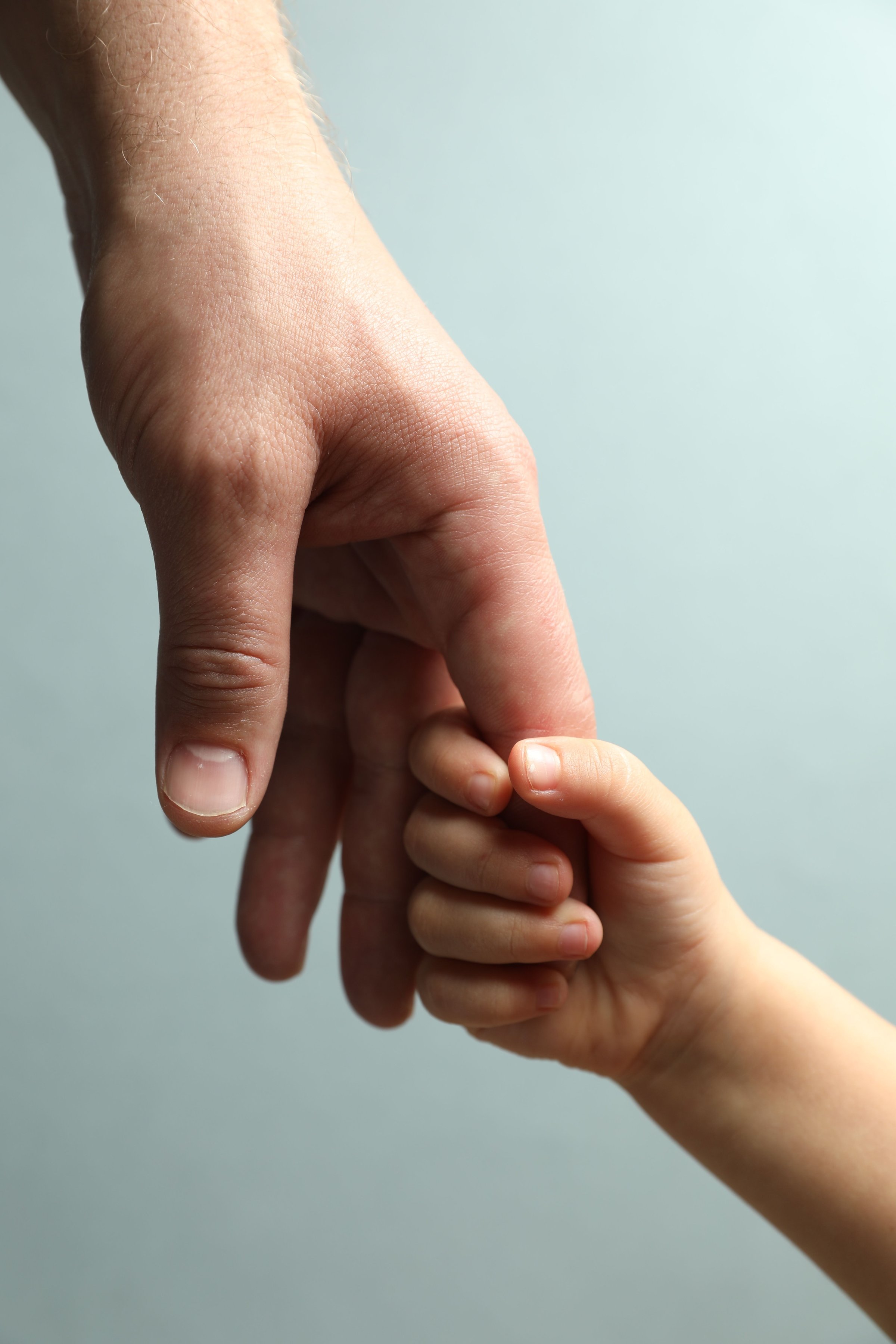Father and child holding hands on light blue background, closeup