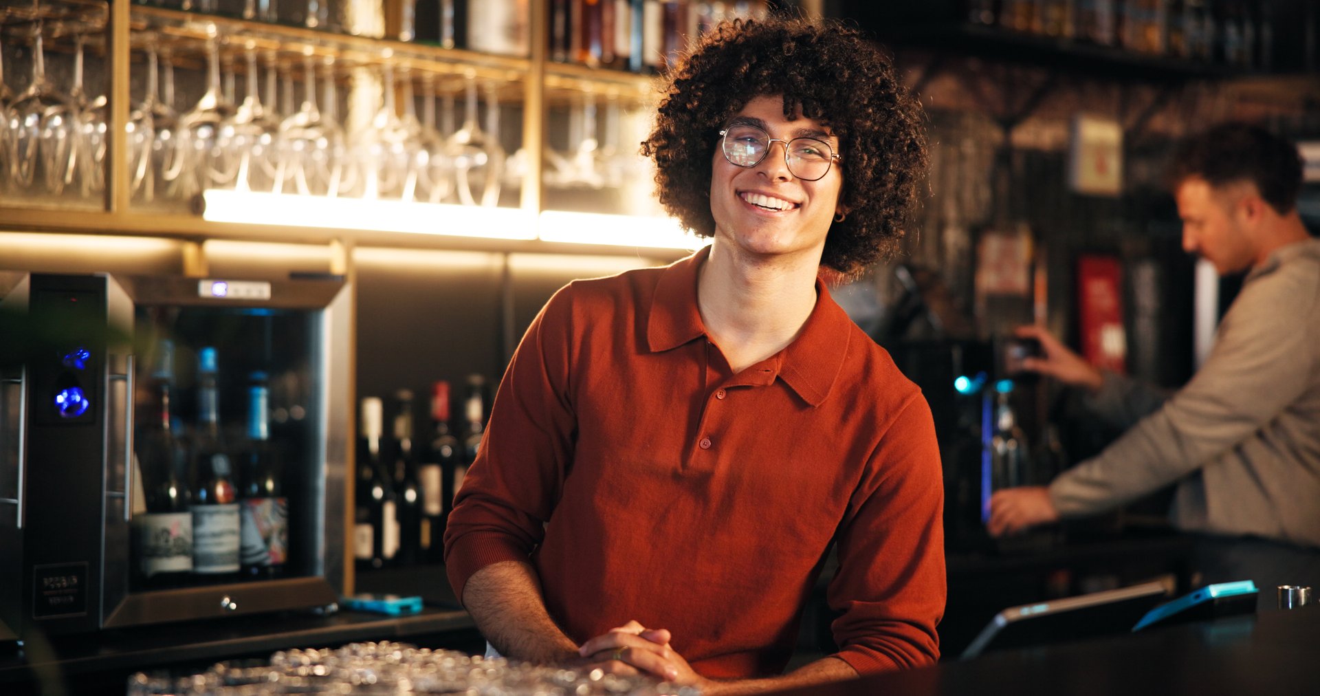 Smile, man and bartender at counter in pub for friendly welcome, customer service and hospitality. Small business, manager and pride at restaurant for taking orders, serving and ready for happy hour