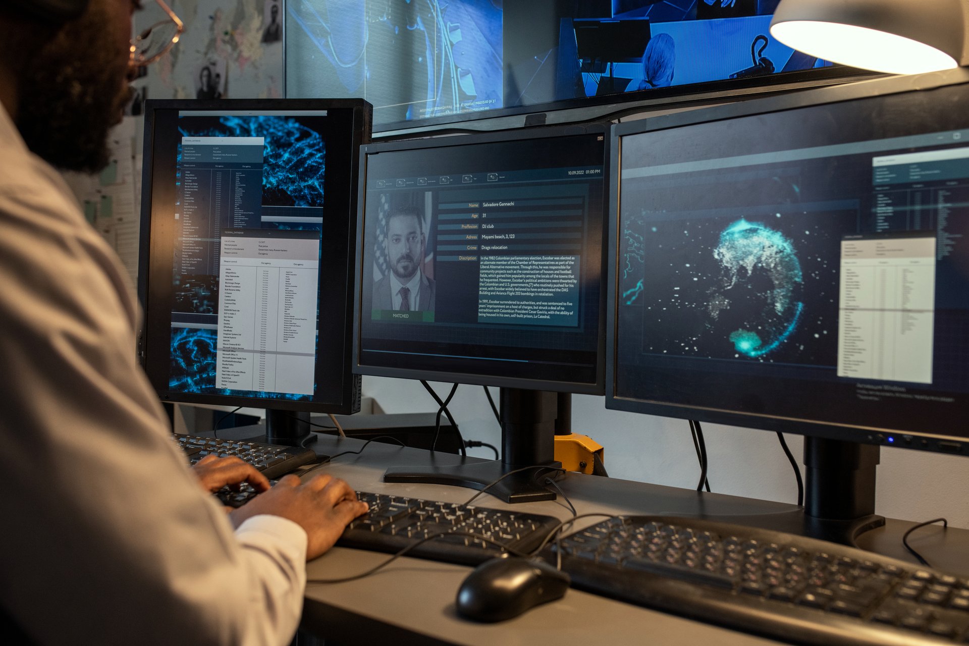 Young policeman entering personal data of suspect into computer database while sitting in front of monitors in office