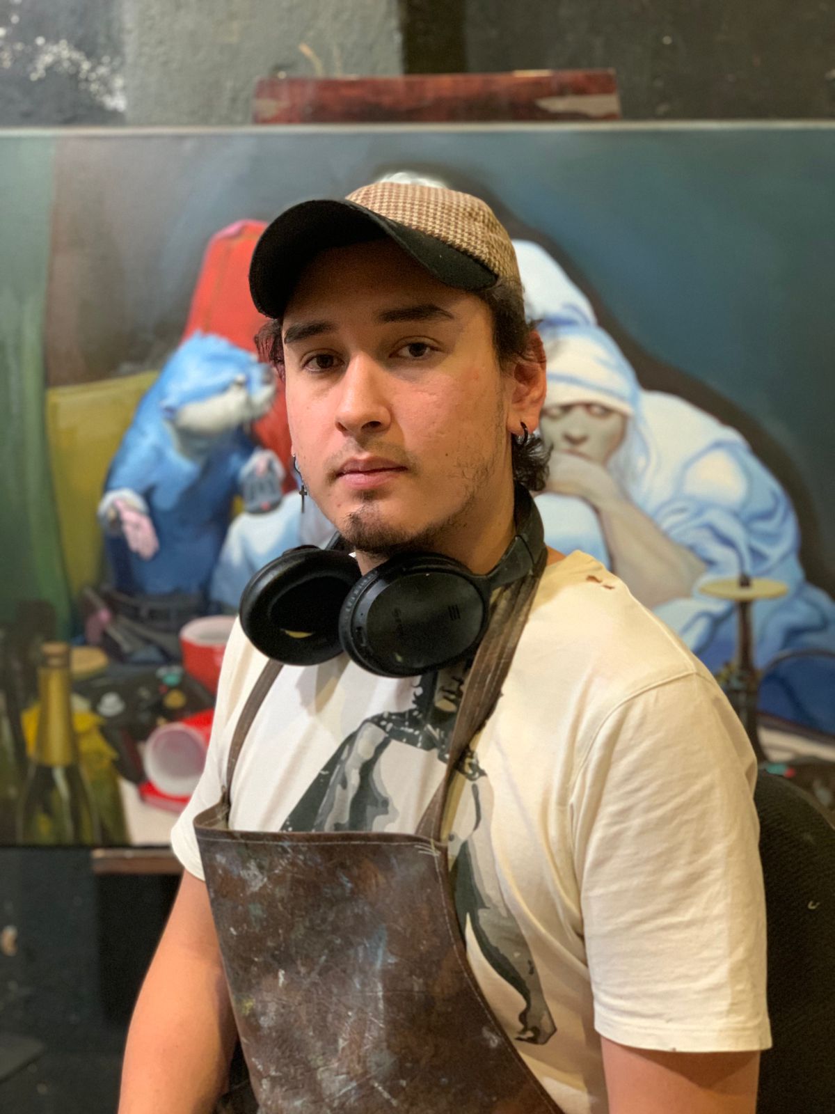 A man in a cap and apron posing in front of an art painting featuring blue and white figures with a monkey.