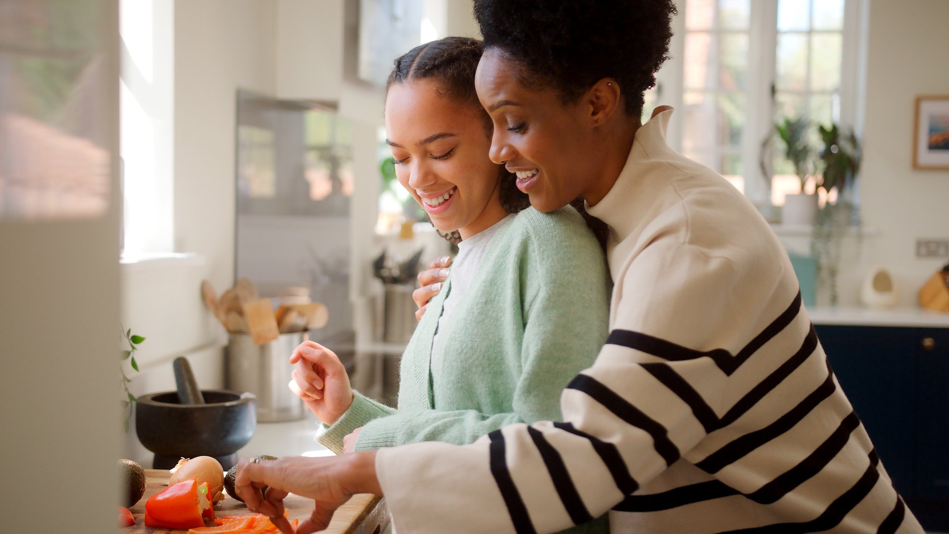 Loving Mother With Teenage Daughter Helping To Prepare Meal At Home In Kitchen Together