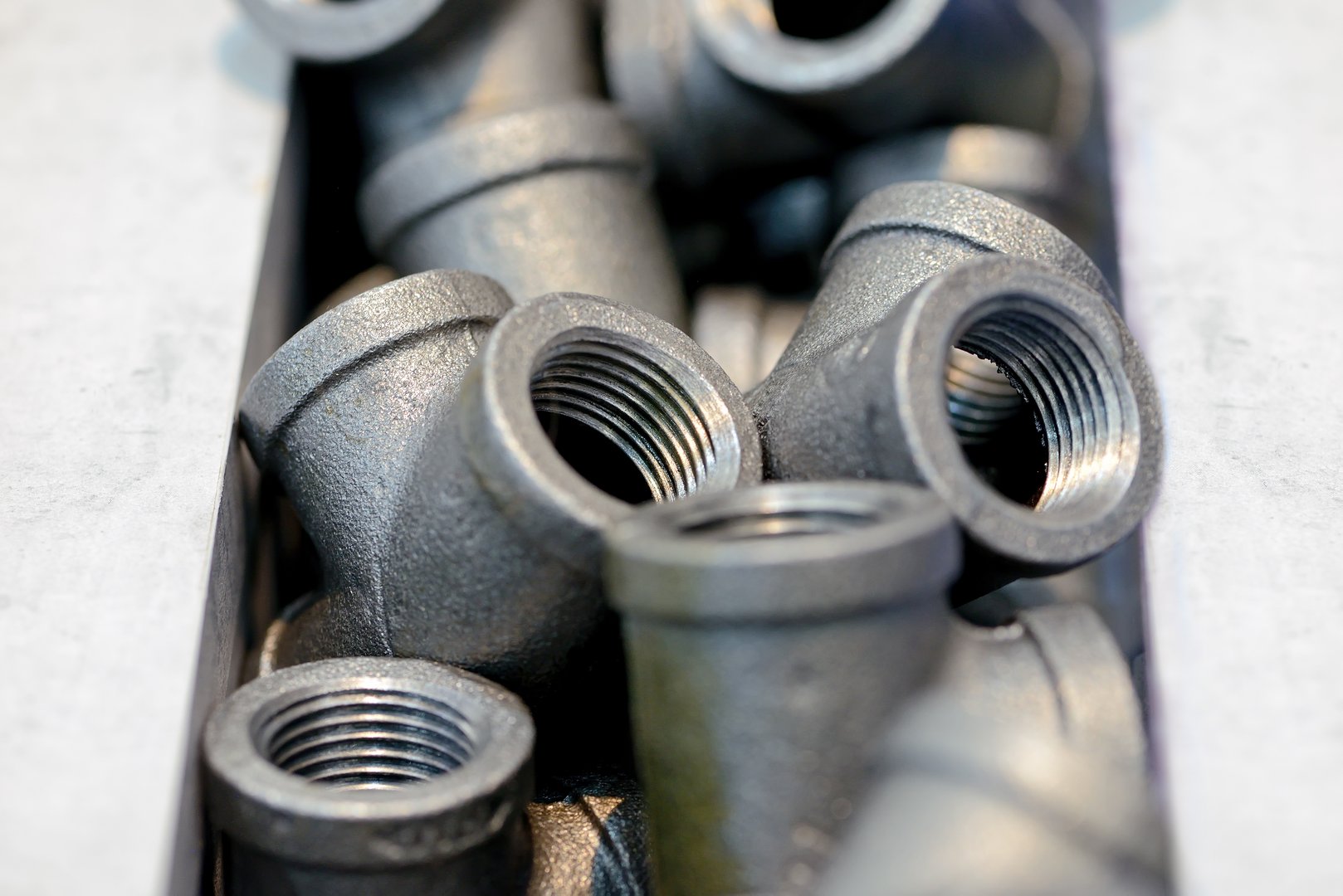 Metal sanitary tees, adapters for water supply pipes lie in a pile. Shallow depth of field.