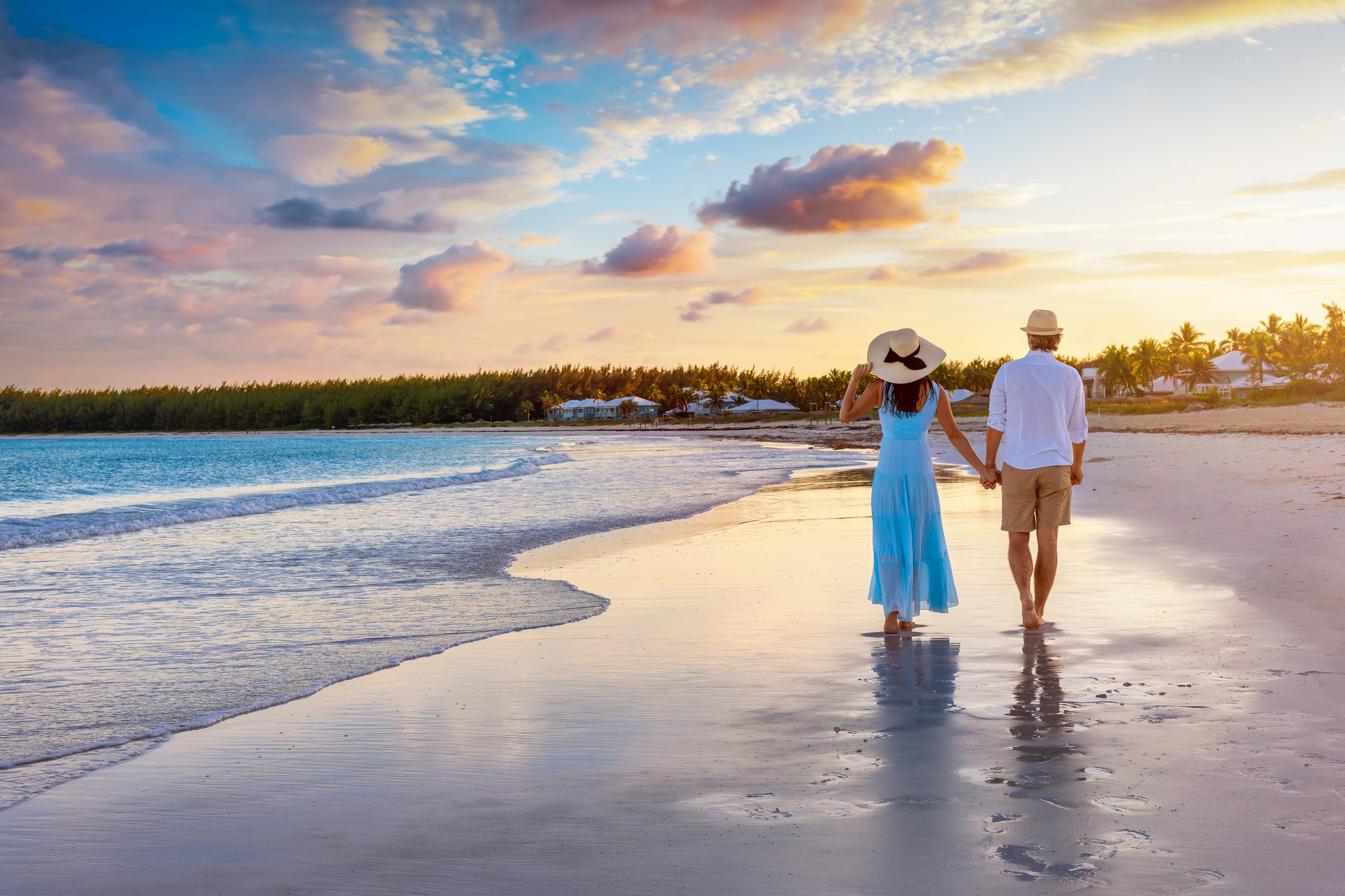 A beautiful couple on vacations walks down a tropical paradise beach during sunset time