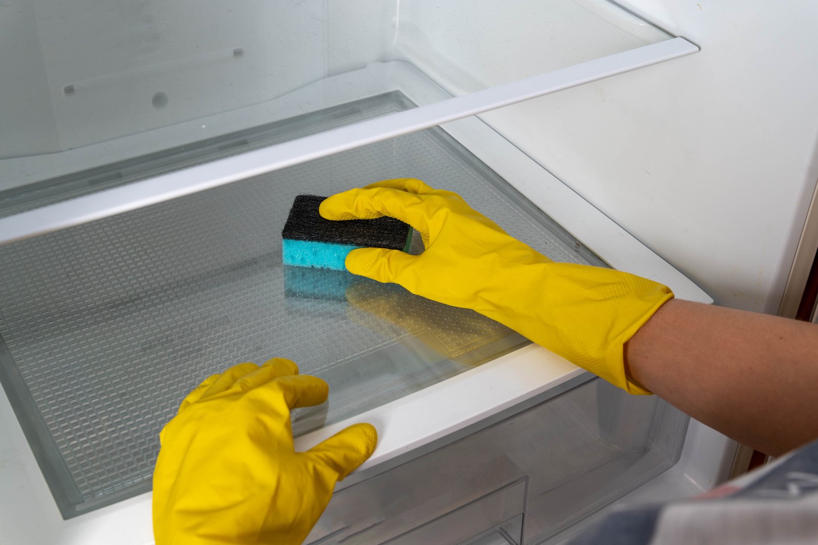 A person is cleaning the inside of a refrigerator with a sponge.
