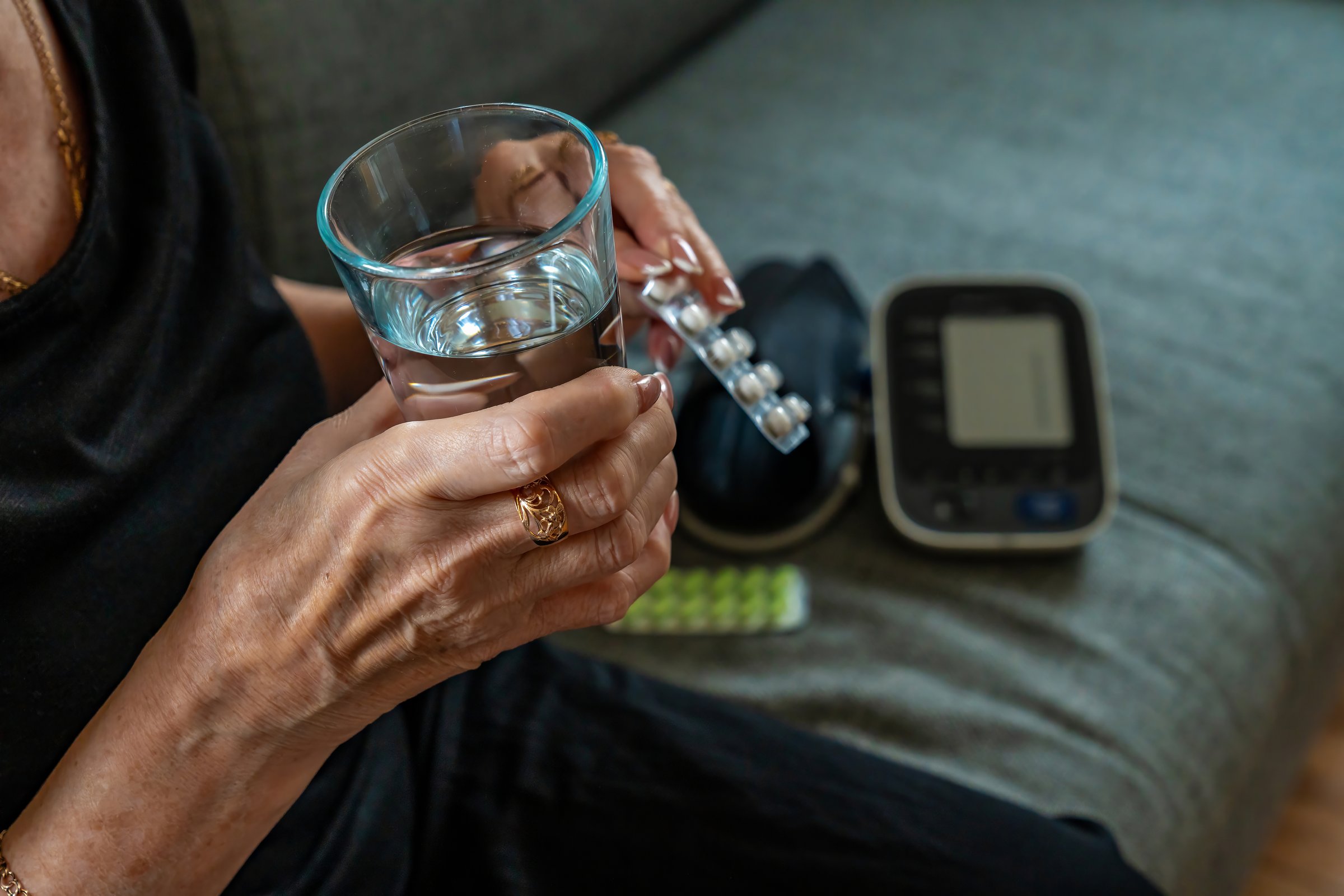 Older adult holding pill and water taking medication near glucose meter on couch with focused motion diabetes selfcare