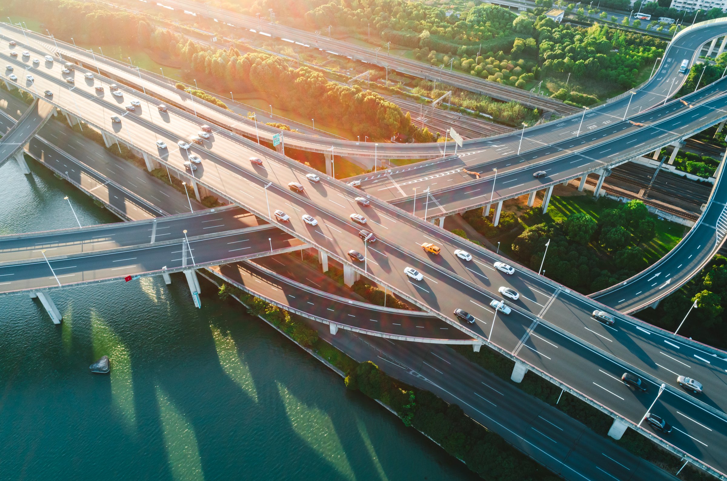 Multiple highways intersect above a calm river, surrounded by vibrant greenery.