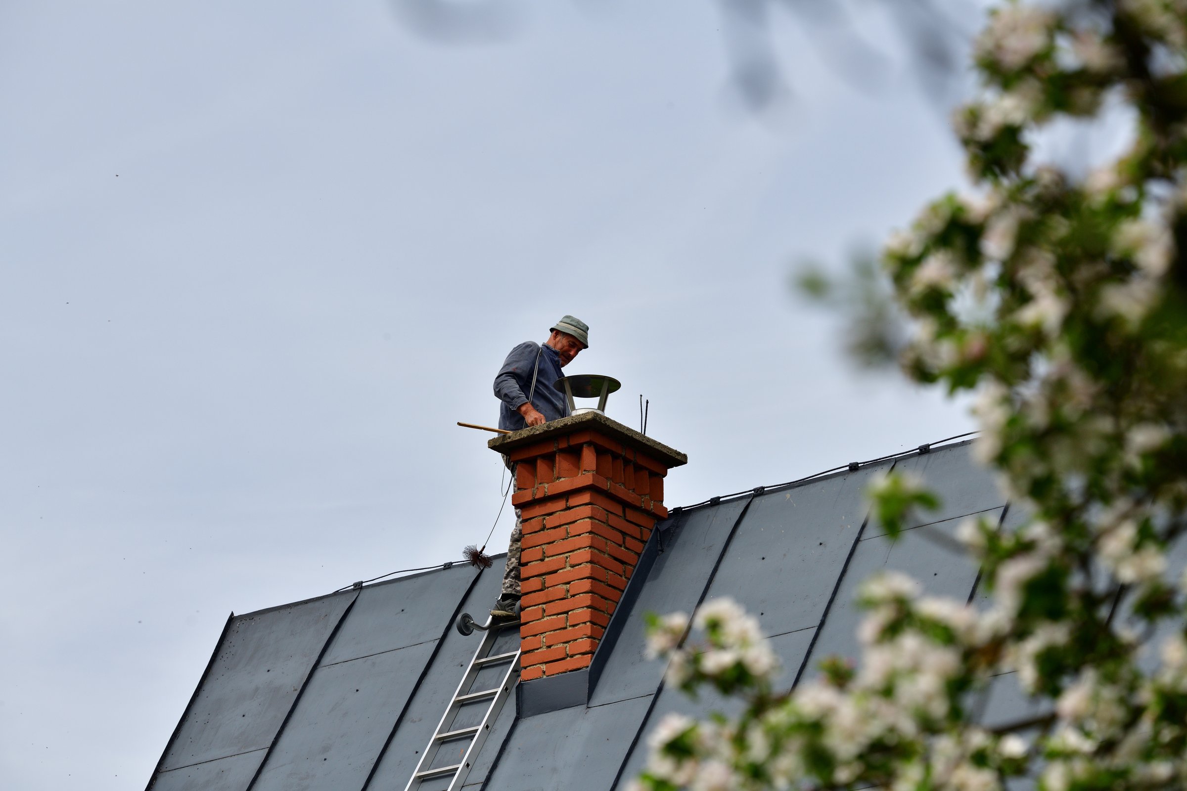 A  chimneyer climbs a ladder to the roof to repair a chimney