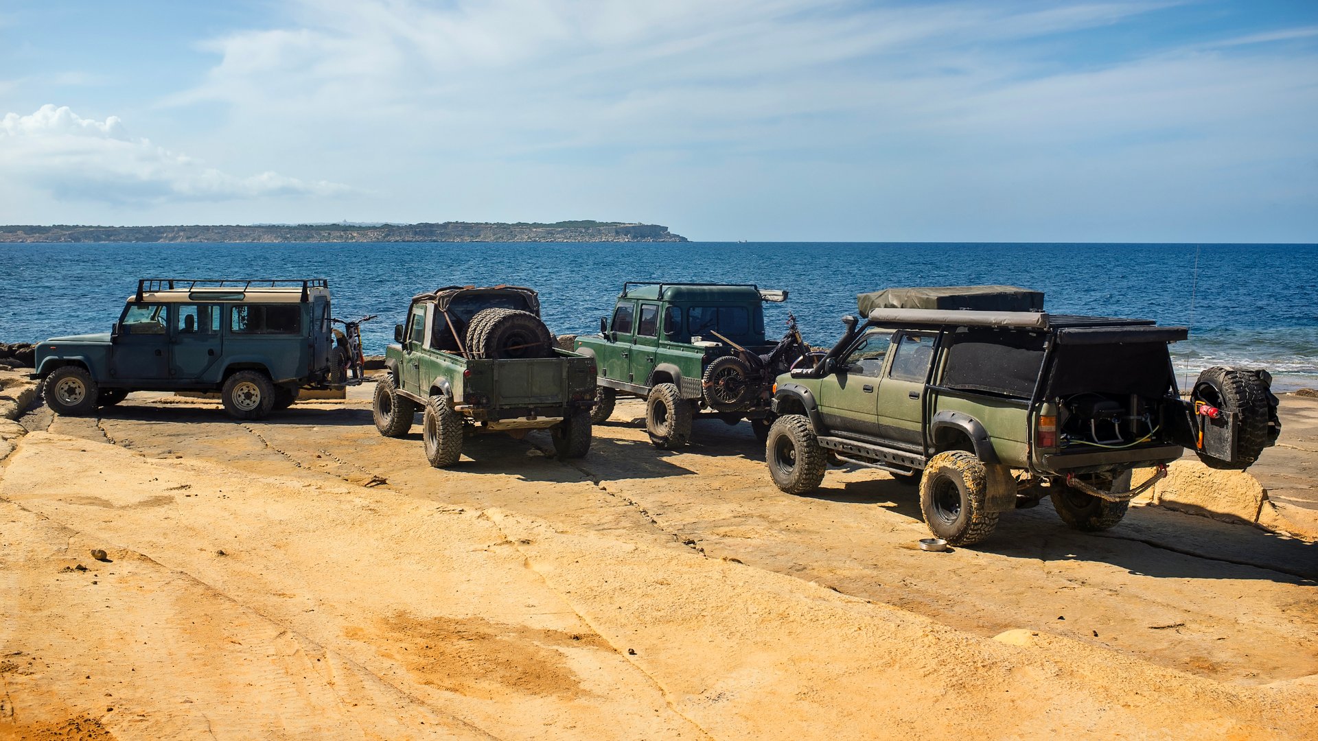 Off-road vehicles with travel gear parked on a rocky coastline. Calm sea and clear sky in the background. Concept of adventure and outdoor travel. Warm tones