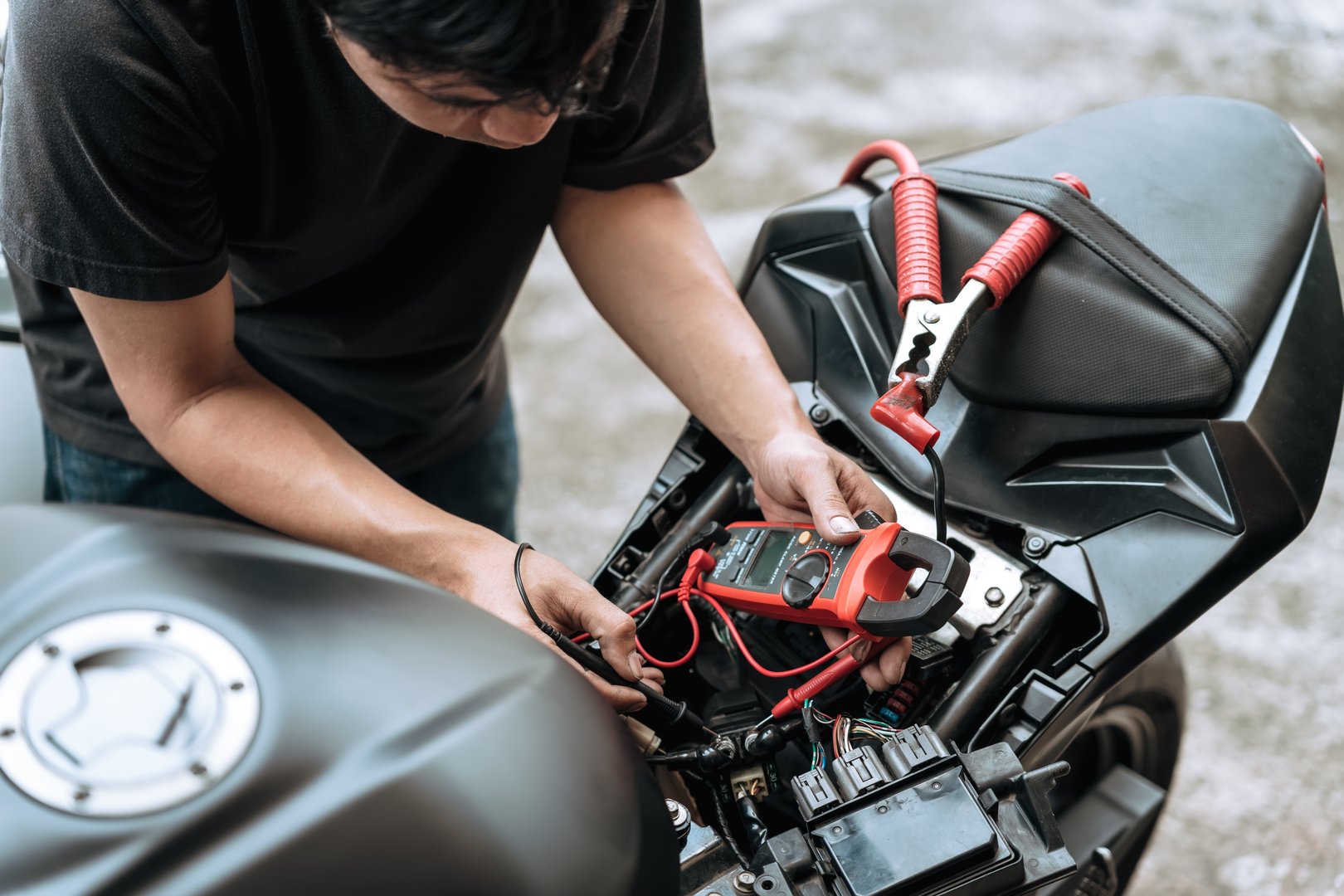 Motorcycle mechanic check motorcycle electrical system,find wiring problems using a multimeter.at garage, motorcycle repair concept