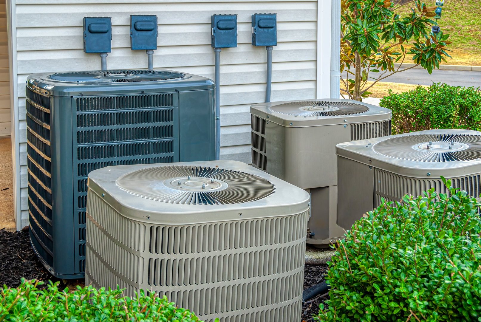 Horizontal shot of four air conditioning units outside of an upscale apartment complex.