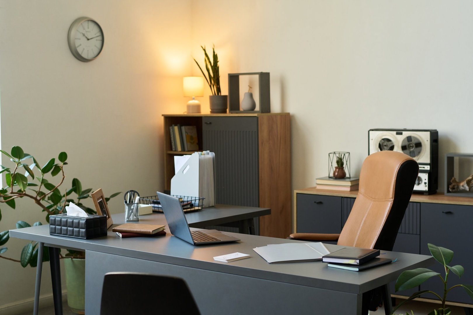 Modern psychologist office interior showing empty workspace with laptop, documents, plants and shelves in background, professional therapy environment prepared for client session
