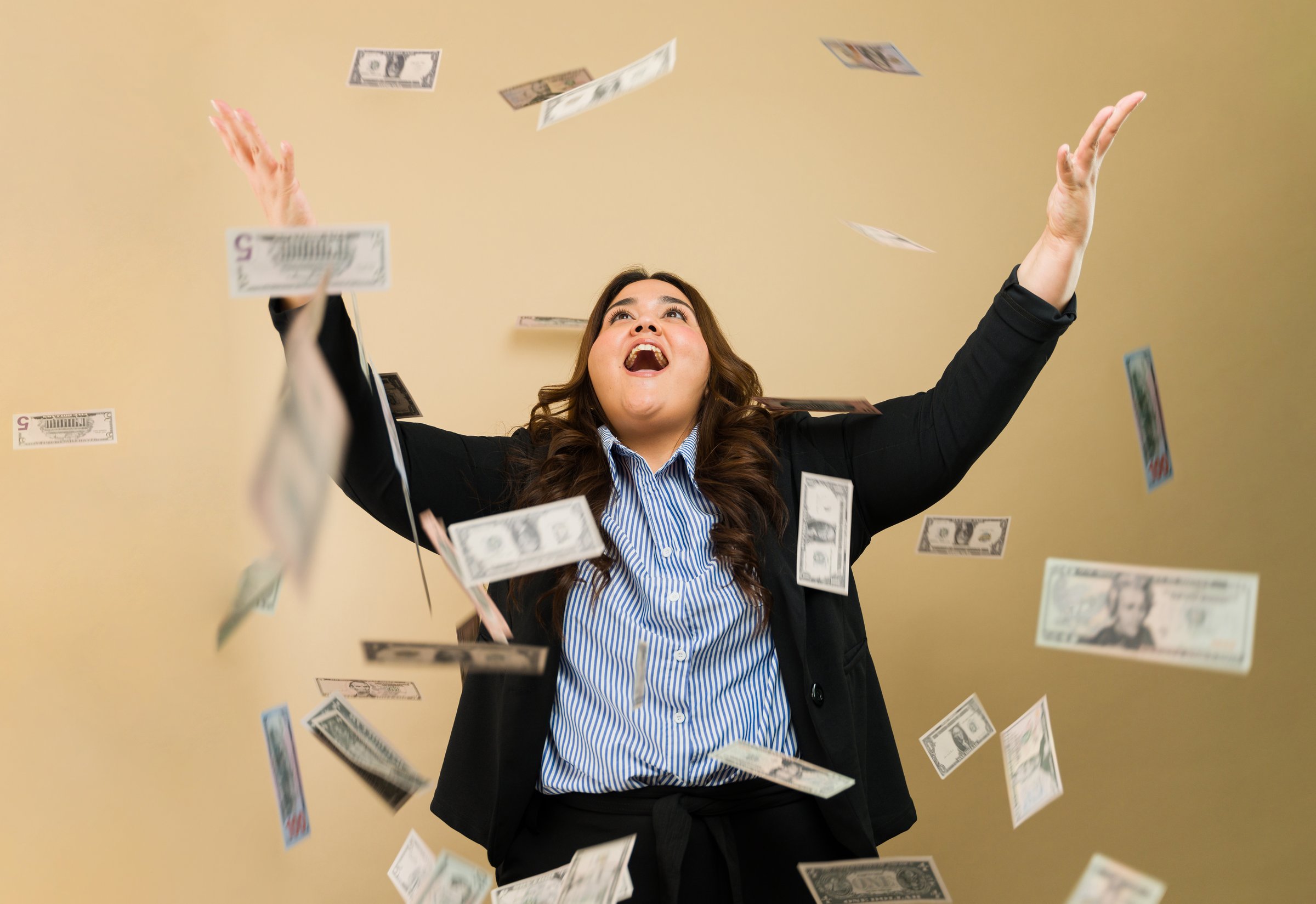 Joyful plus-size woman in business attire surrounded by flying money in a studio environment