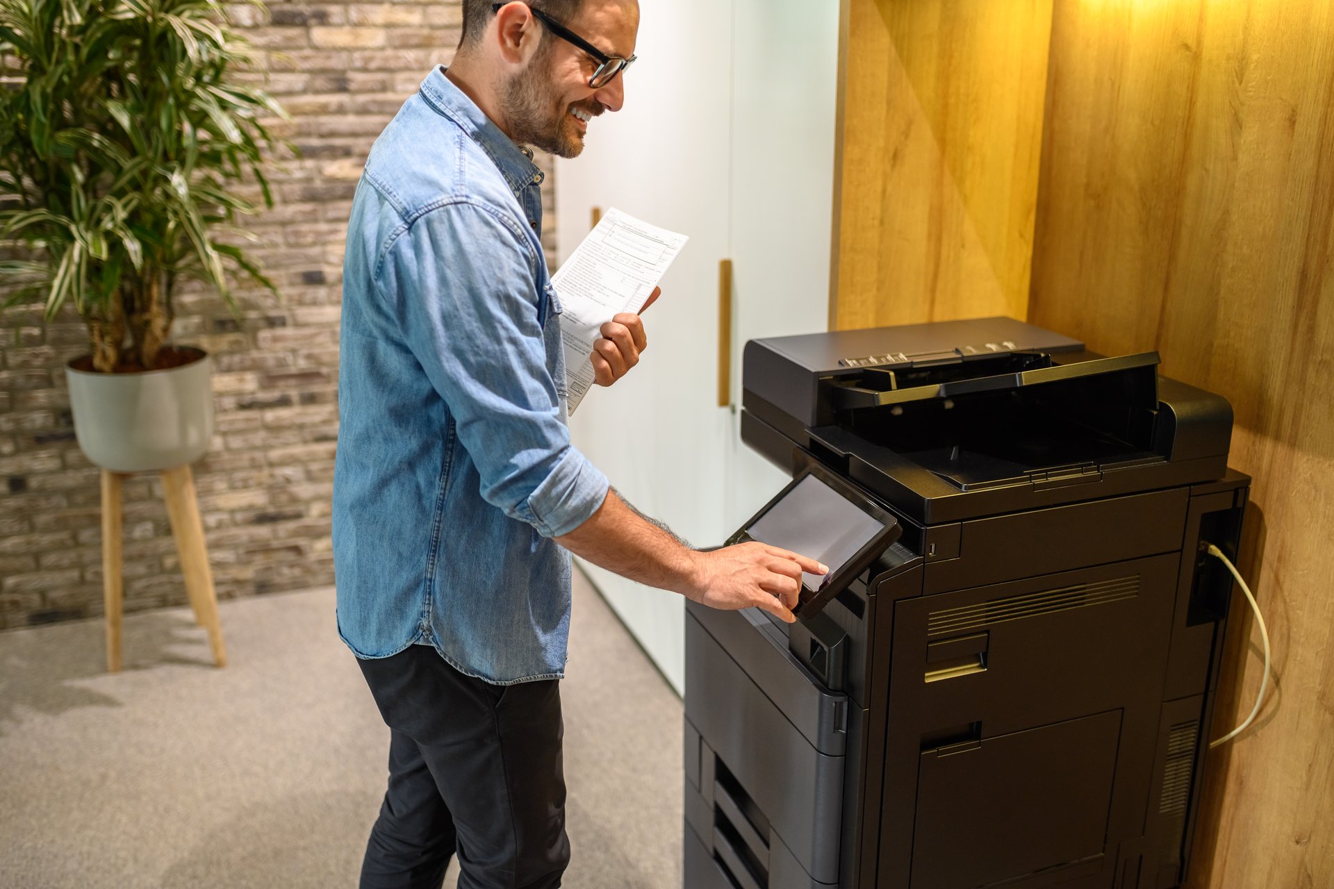 Midsection of happy project manager holding documents and operating photocopier at modern workplace