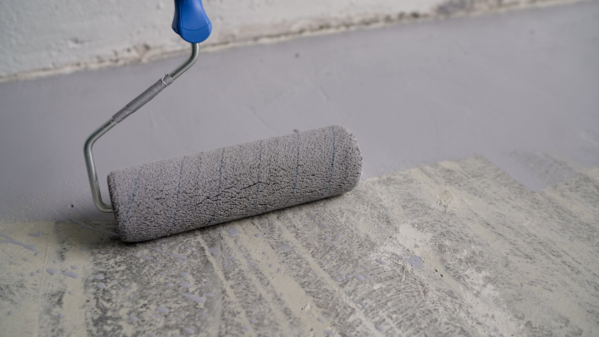 Close-up of a roller used to paint a floor. Close-up of primer being applied to the floor. Close-up of a construction worker applying gray epoxy resin in an industrial workshop.