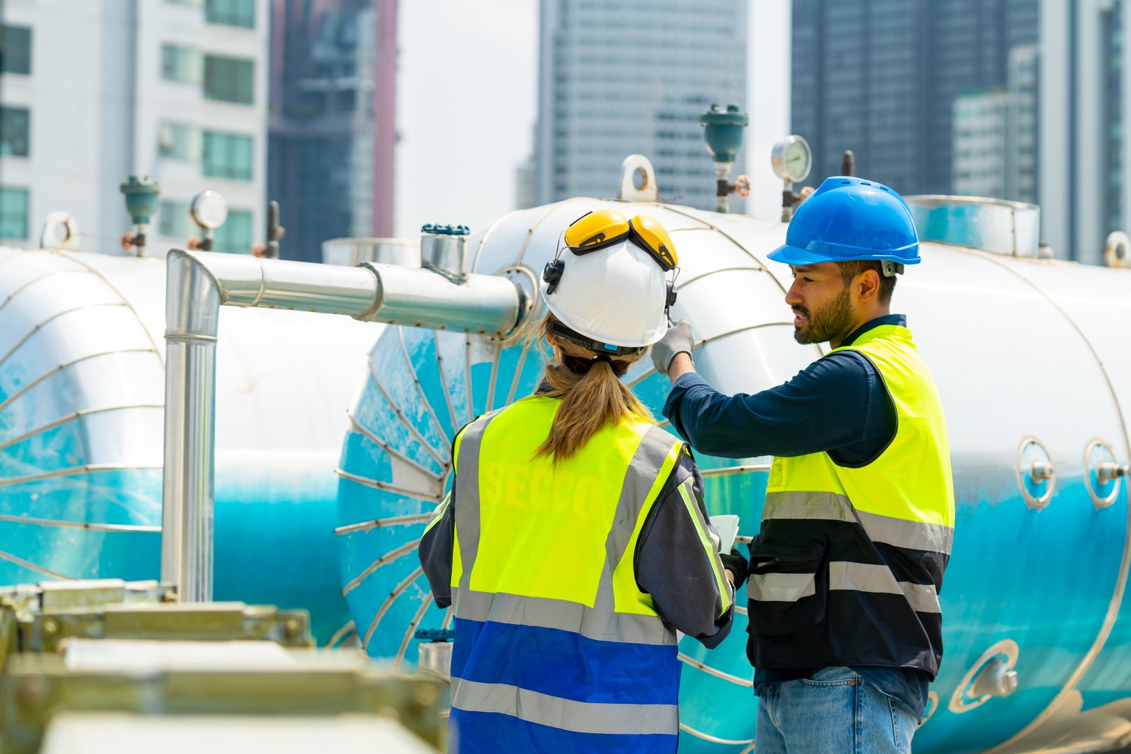 Professional Asian man and woman teamwork engineer in safety uniform working at outdoor construction site rooftop. Industrial technician worker maintenance checking building exterior plumbing system.