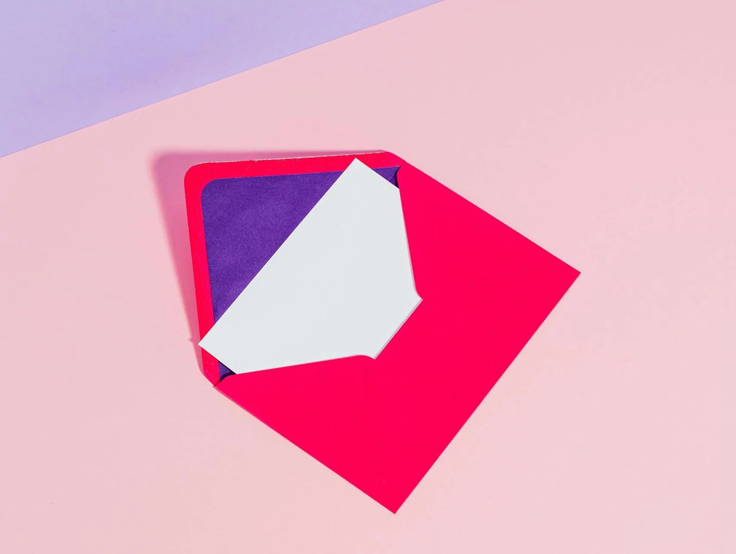 A red envelope partially open with a blank white card inside, set on a pastel pink and purple background.