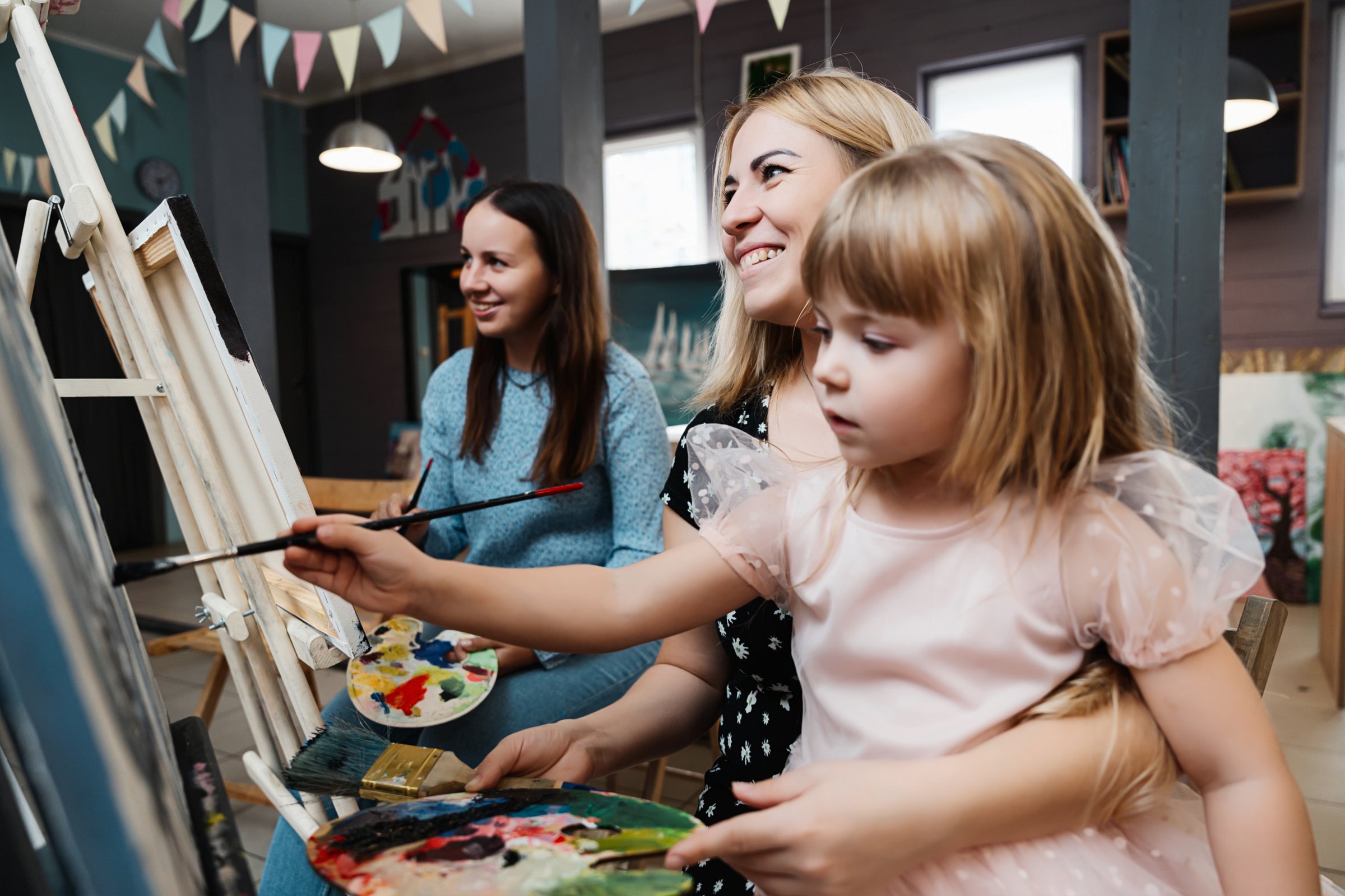 A woman and her daughter joyfully paint together in a bright studio.