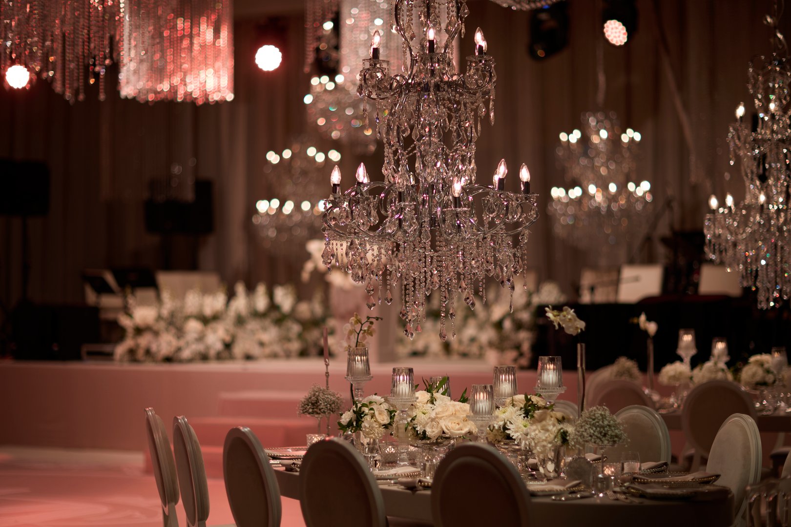 An exquisite close-up of a luxurious wedding table setup featuring a stunning crystal chandelier, elegant floral arrangements, and candlelit decorations. Perfect for showcasing wedding inspiration, event design, or luxury dining themes.