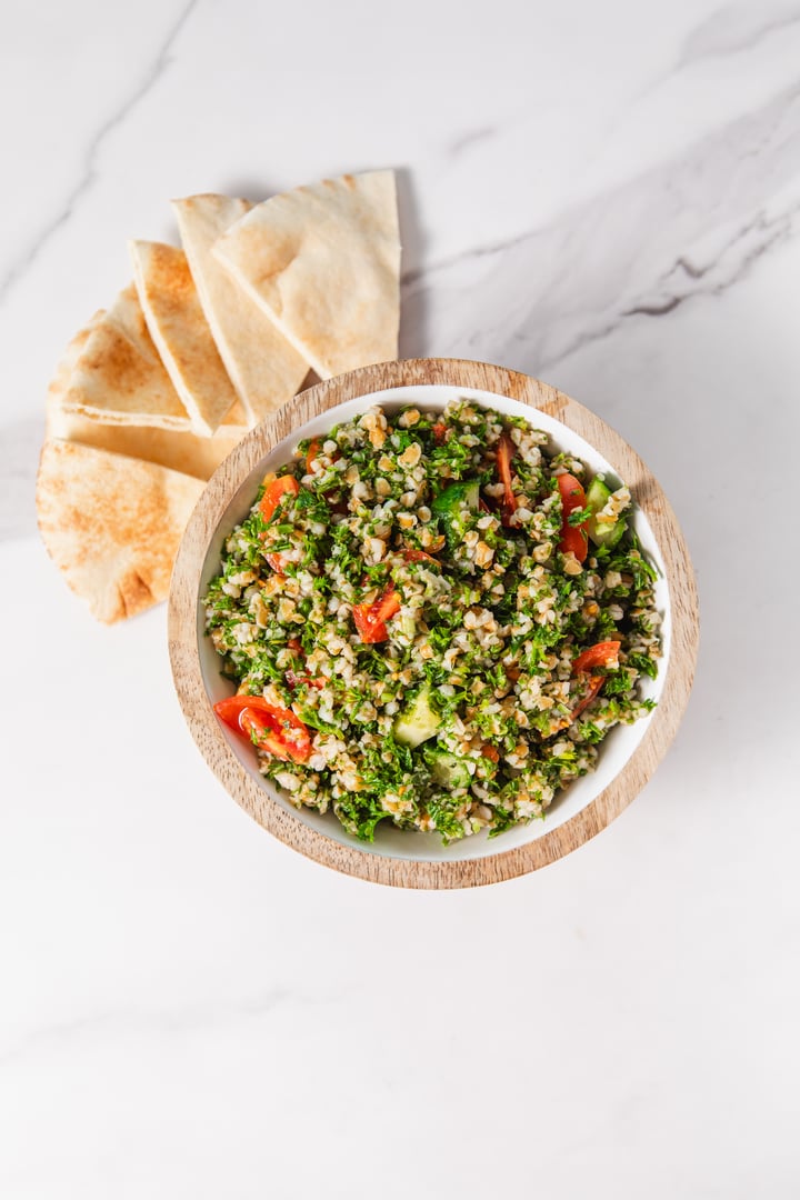 Tabbouleh Salad with Tomatoes in wooden bowl and pita bread on marble background. High quality photo taken top down view on Canon 5D Mark II and edited in Adobe Lightroom.