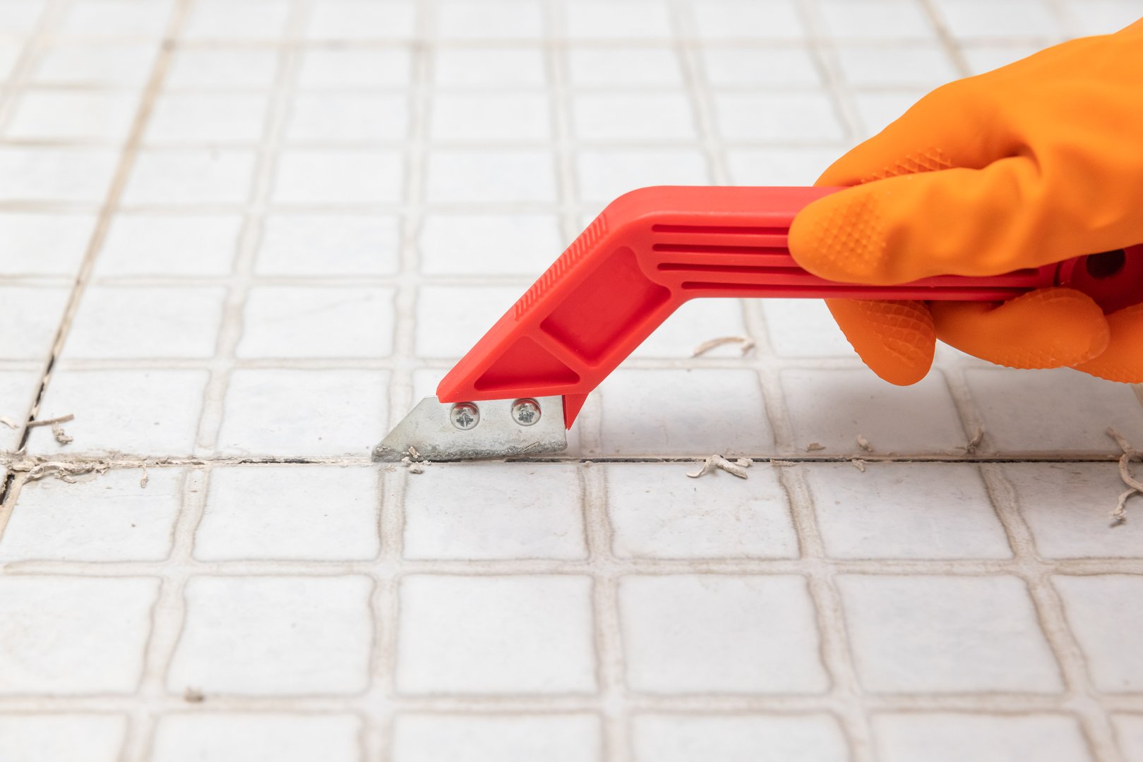 Housekeeper remove old grout from bathroom tiles.  Raking out grout tiles for regrouting.