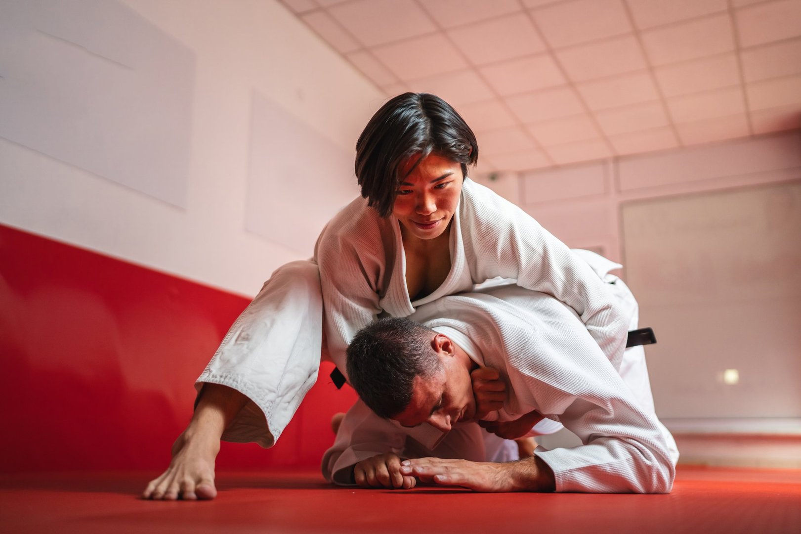 Two judokas practicing grappling techniques on a tatami mat, with the man executing a hold-down on the man, demonstrating skill and control in a martial arts training session