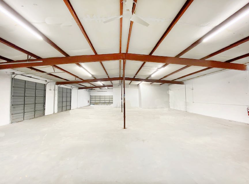 Spacious empty warehouse interior with white walls, concrete floor, and exposed metal beams, featuring multiple garage doors.