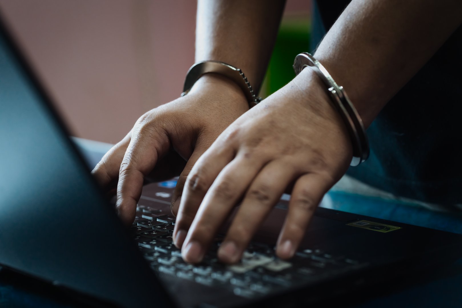 Cybercrime arrest concept. Close-up of a hacker in handcuffs typing on a laptop, symbolizing internet fraud, data theft, and online security risks in the digital world.