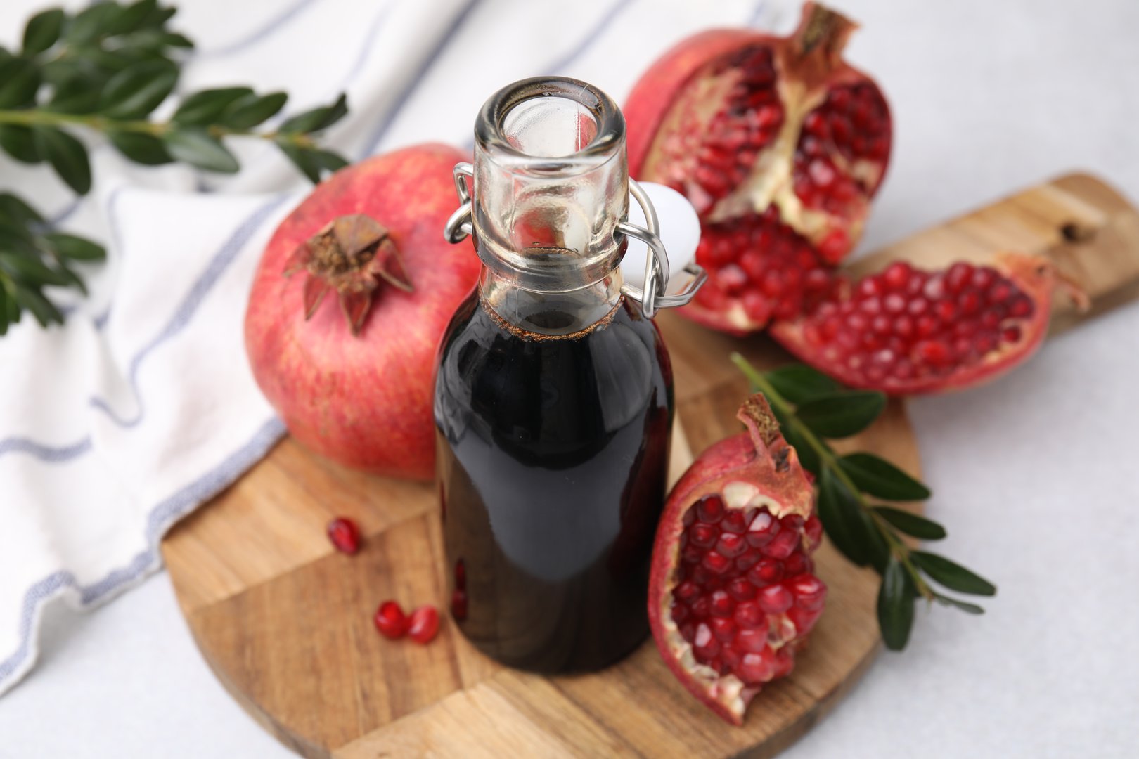 Tasty pomegranate sauce in bottle, branches and fruits on light table, closeup