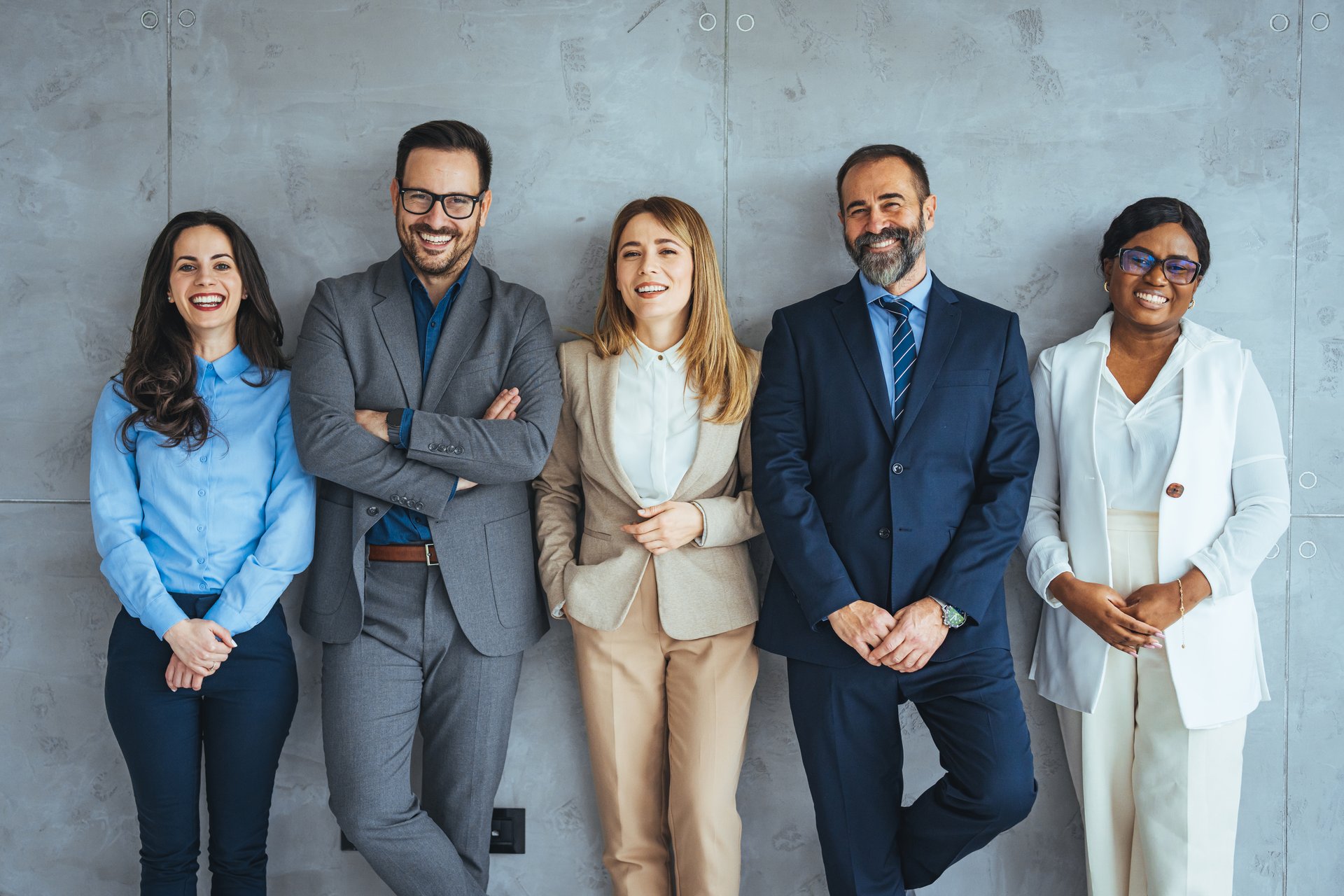 Studio portrait of a group of businesspeople posing against a gray background. Portrait of multi-ethnic male and female professionals. Business colleagues are standing against wall.