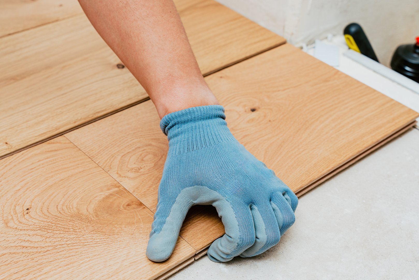 Worker installer wearing blue gloves carefully aligns wooden floor planks, ensuring smooth and accurate installation