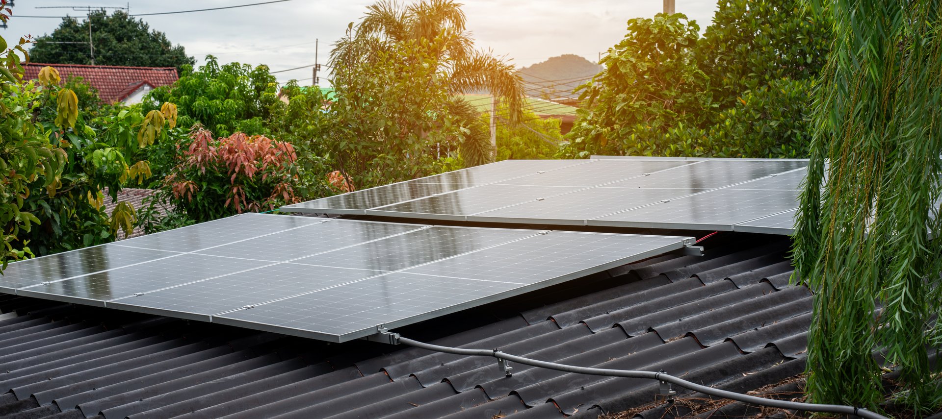 Solar panels installed on a house roof surrounded by lush green trees, clean renewable energy concept in a natural environment.