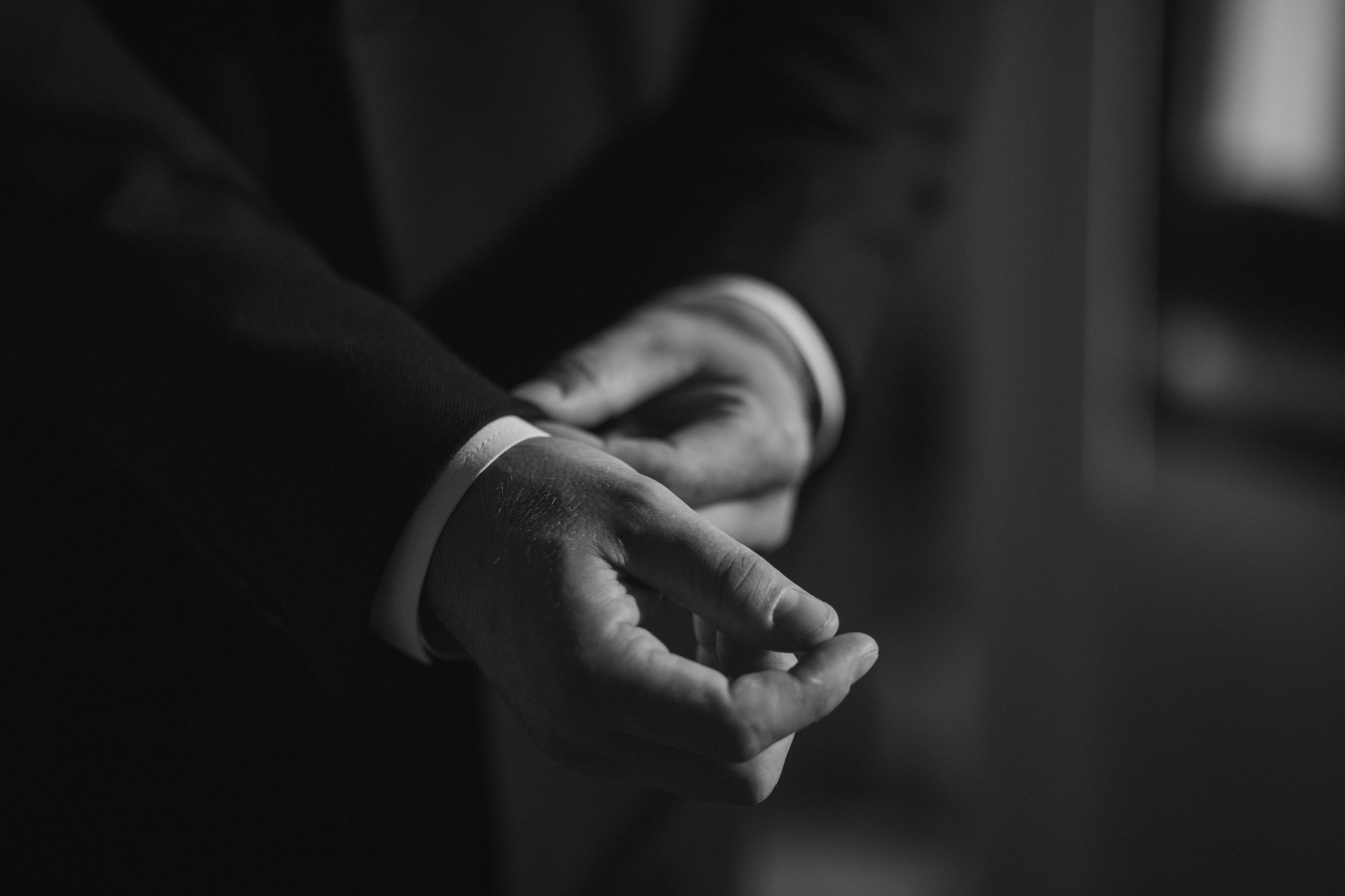 Hands adjusting cufflinks on a suit jacket in black and white.
