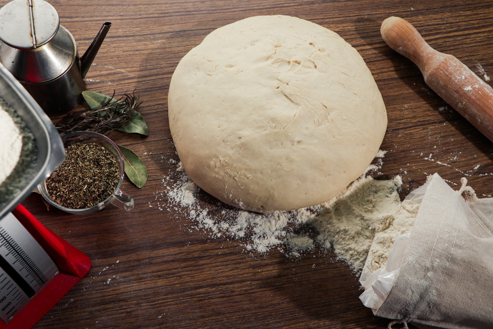 top view. pizza dough, together with the rolling pin, flour sack, scales, oil and oregano.