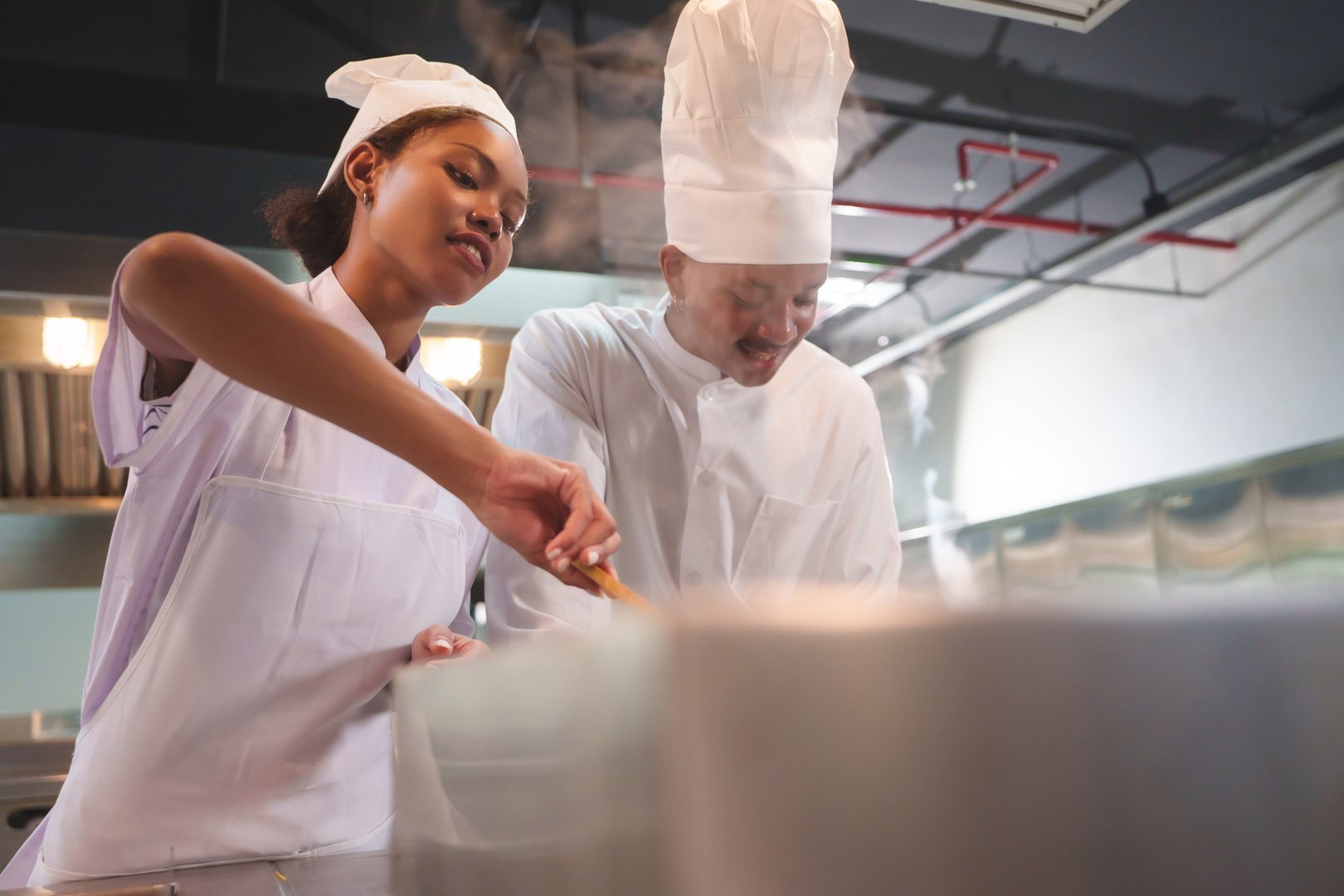 Closeup of African American female chef stirring pot with Black male chef assisting, teamwork in modern kitchen