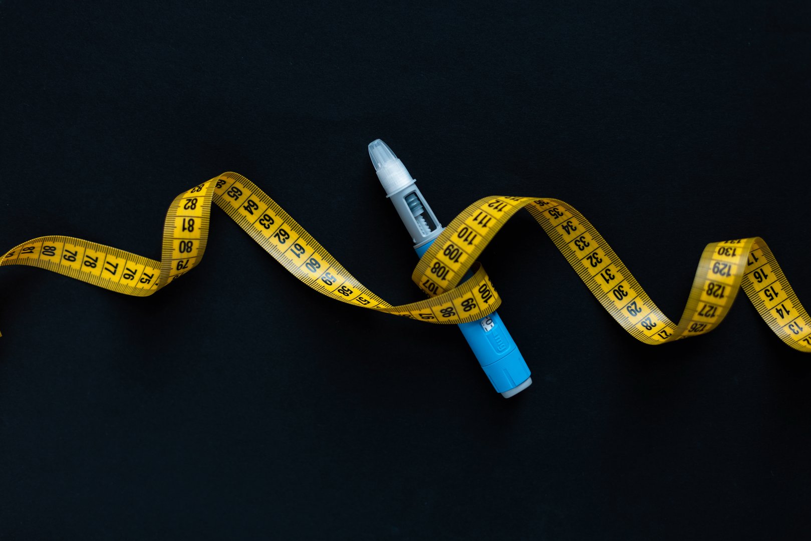 Insulin injection pen wrapped in measuring tape, symbolizing obesity treatment, diabetic care, and health control, set against a minimalistic black background. Ozempic injection for diabetes