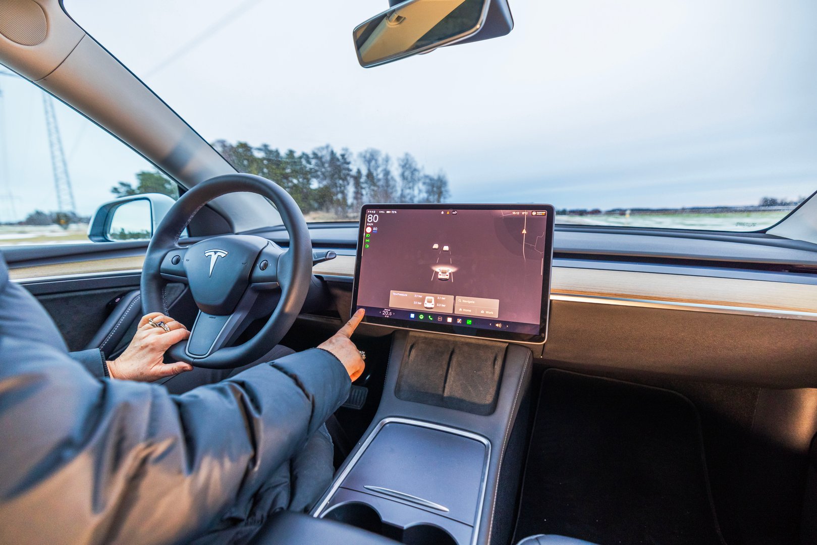 Sweden. Uppsala. 01.21.2025. Tesla Model Y driver interacting with touchscreen display, showcasing vehicle settings, navigation and autonomous driving features.