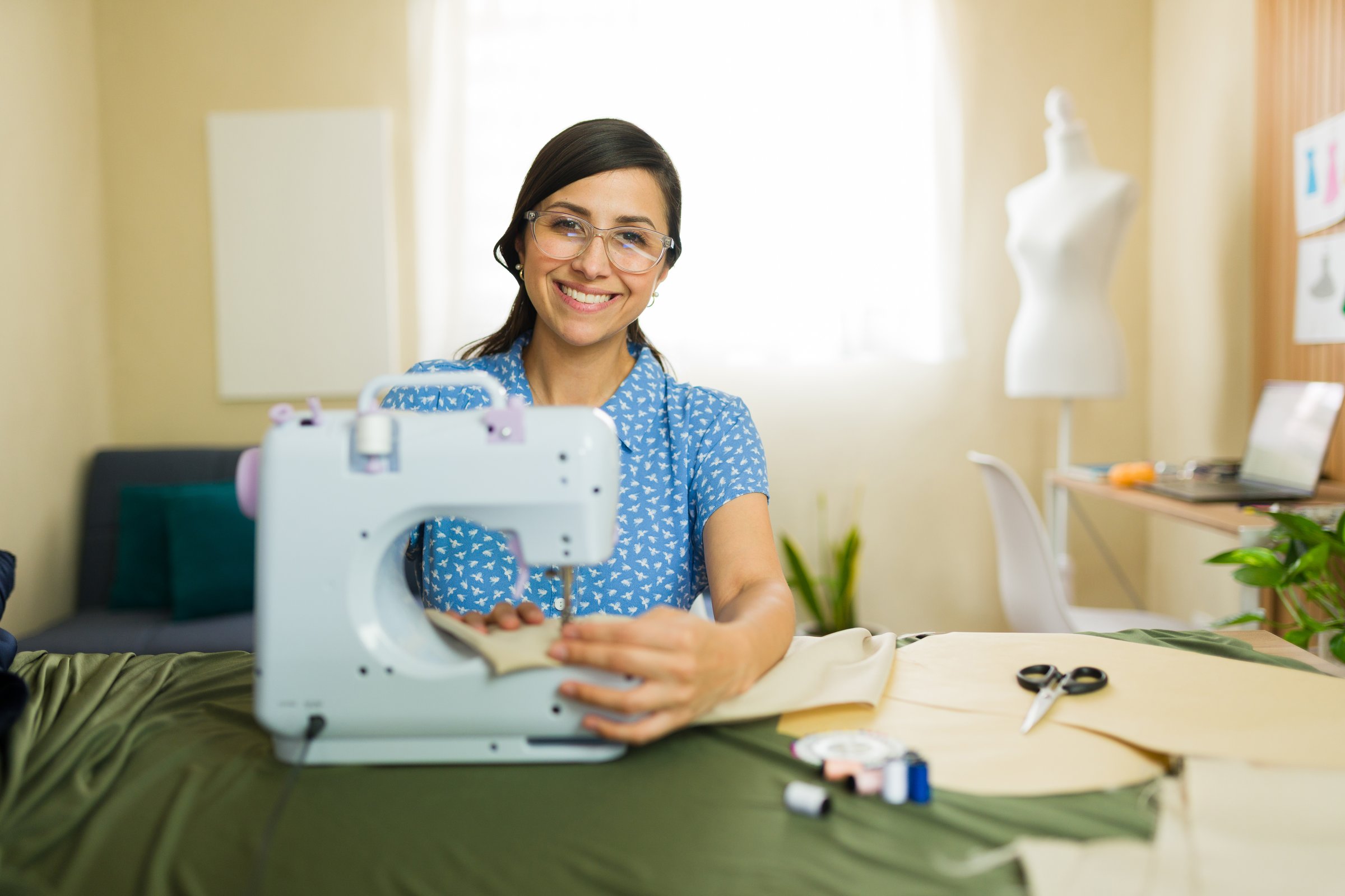 Happy entrepreneur working from home and using a sewing machine to create clothes in her small business studio