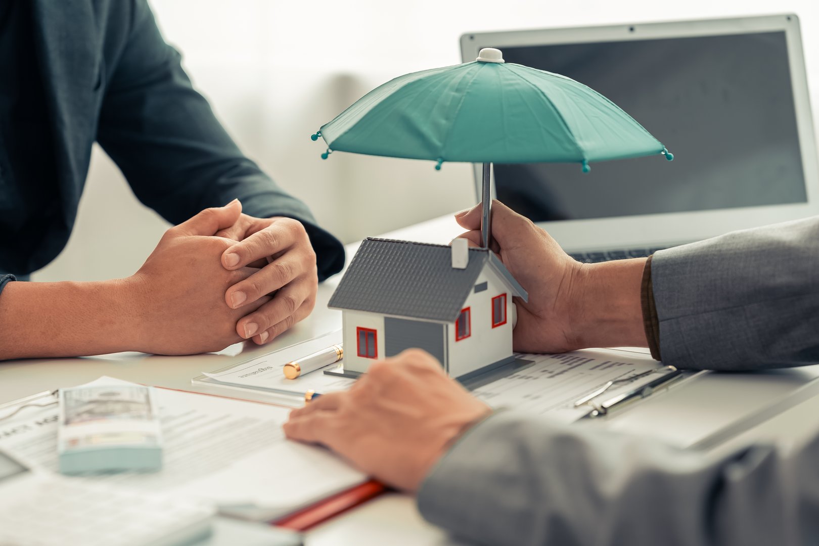 Male home insurance agent holding an umbrella covering his house advising customers about the concept of property and real estate insurance.