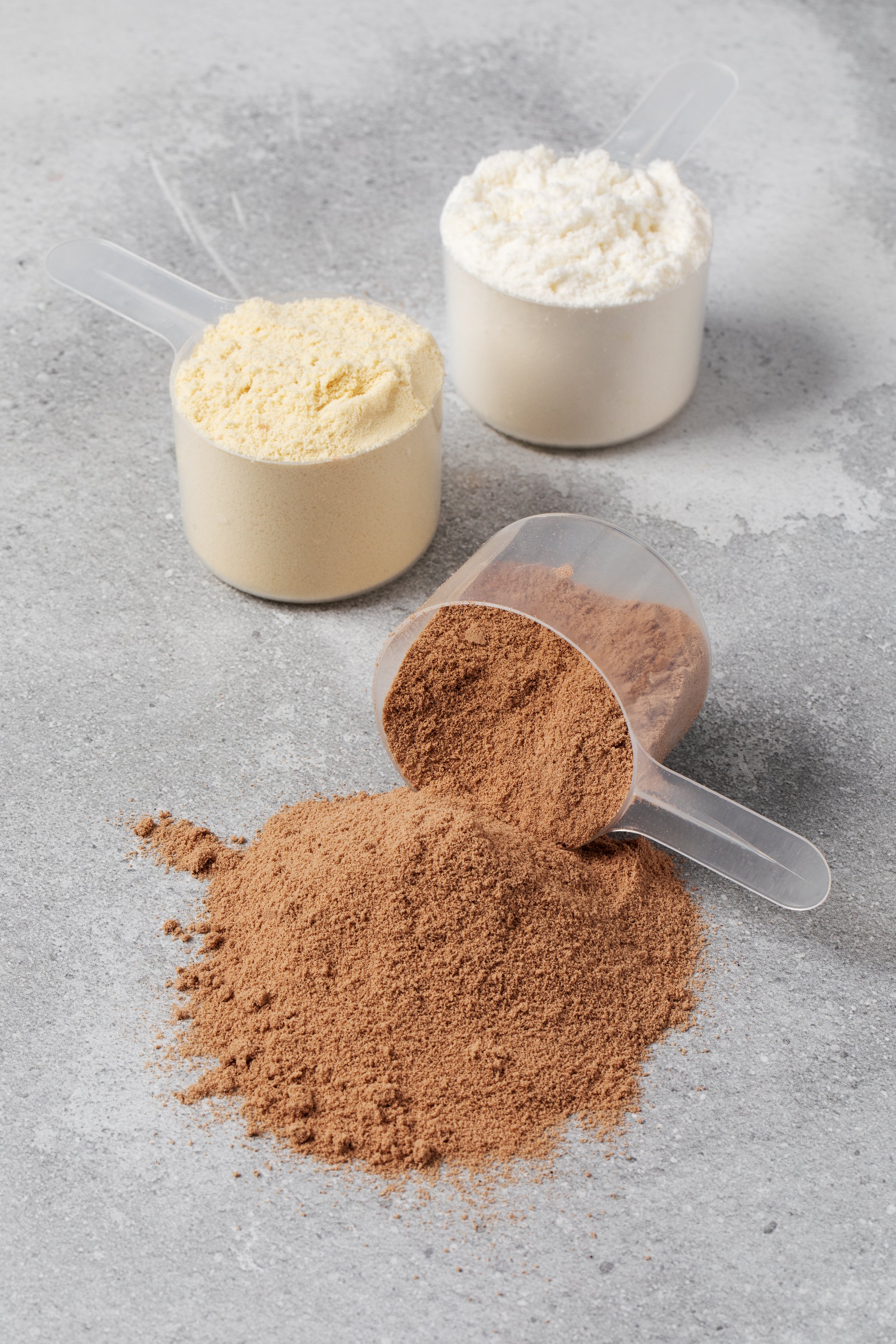 Various protein powders in scoops on gray background for fitness and nutrition. Sport drink.