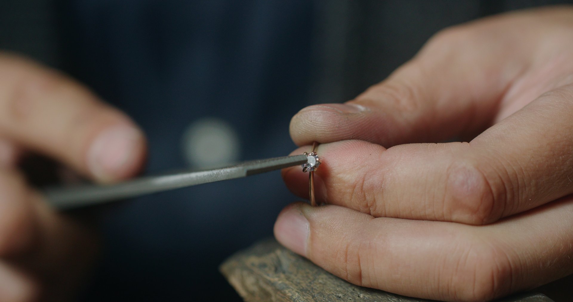 Real time closeup of crop anonymous male specialist using file while shaping place for gemstone in ring during work in professional studio