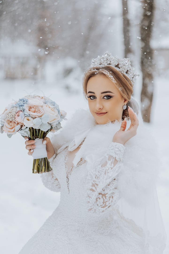 A woman in a white dress is holding a bouquet of flowers and wearing a tiara. She is posing for a photo in the snow