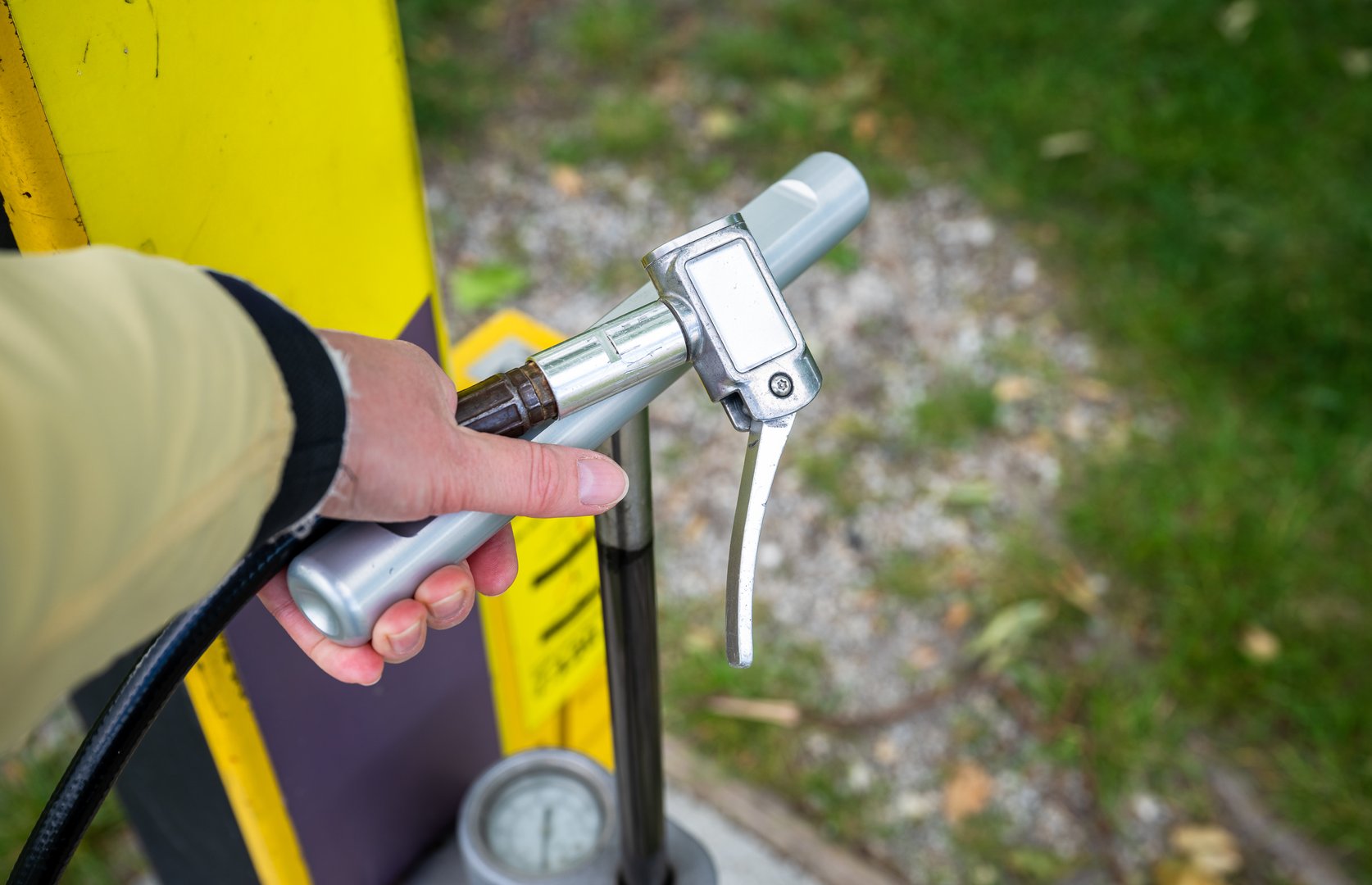Hand using public bicycle air pump to inflate tire at outdoor repair station in city park