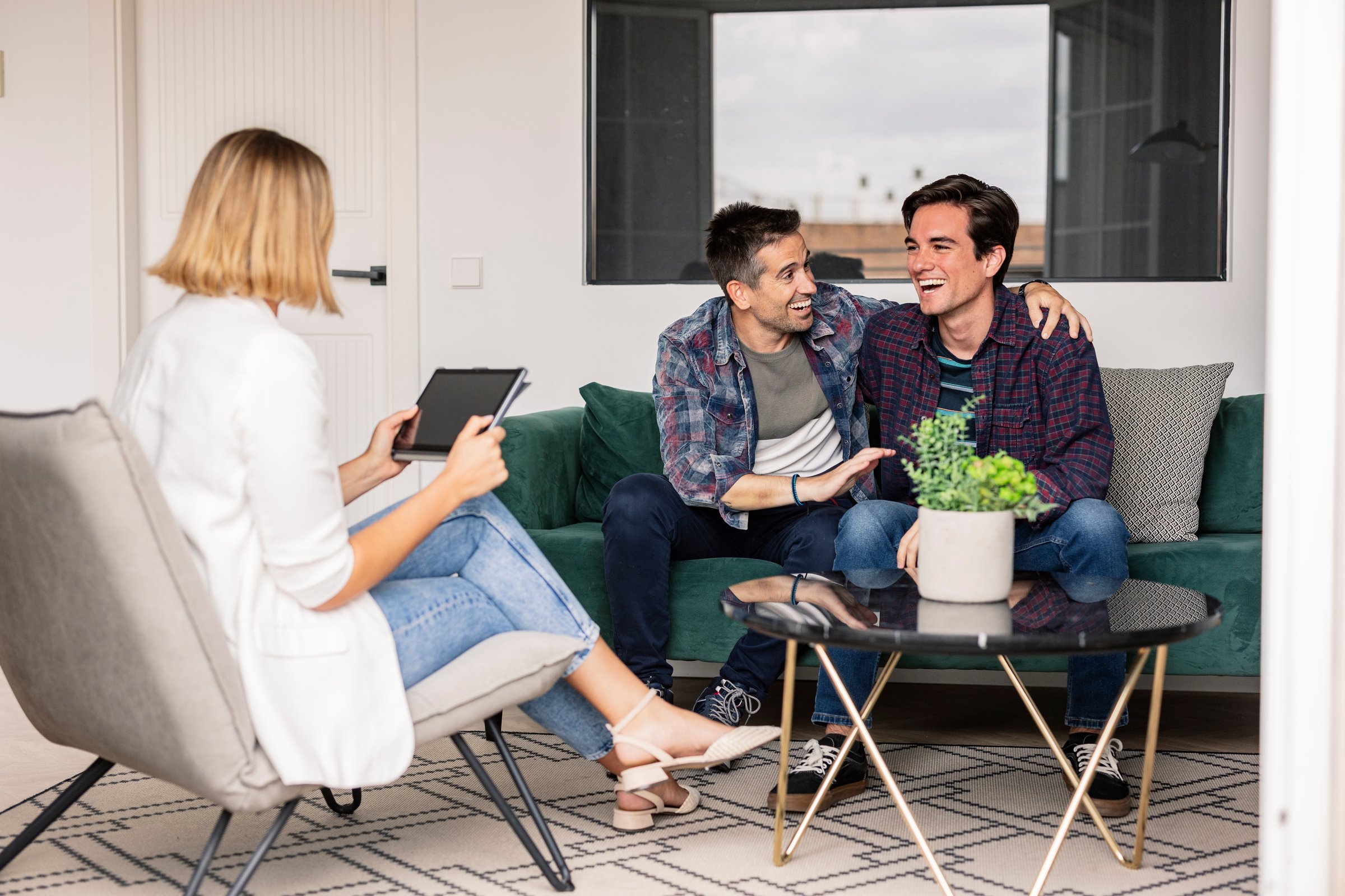 Loving gay couple in therapy with a caring therapist in a cozy living room, deep in conversation, sharing smiles and laughter