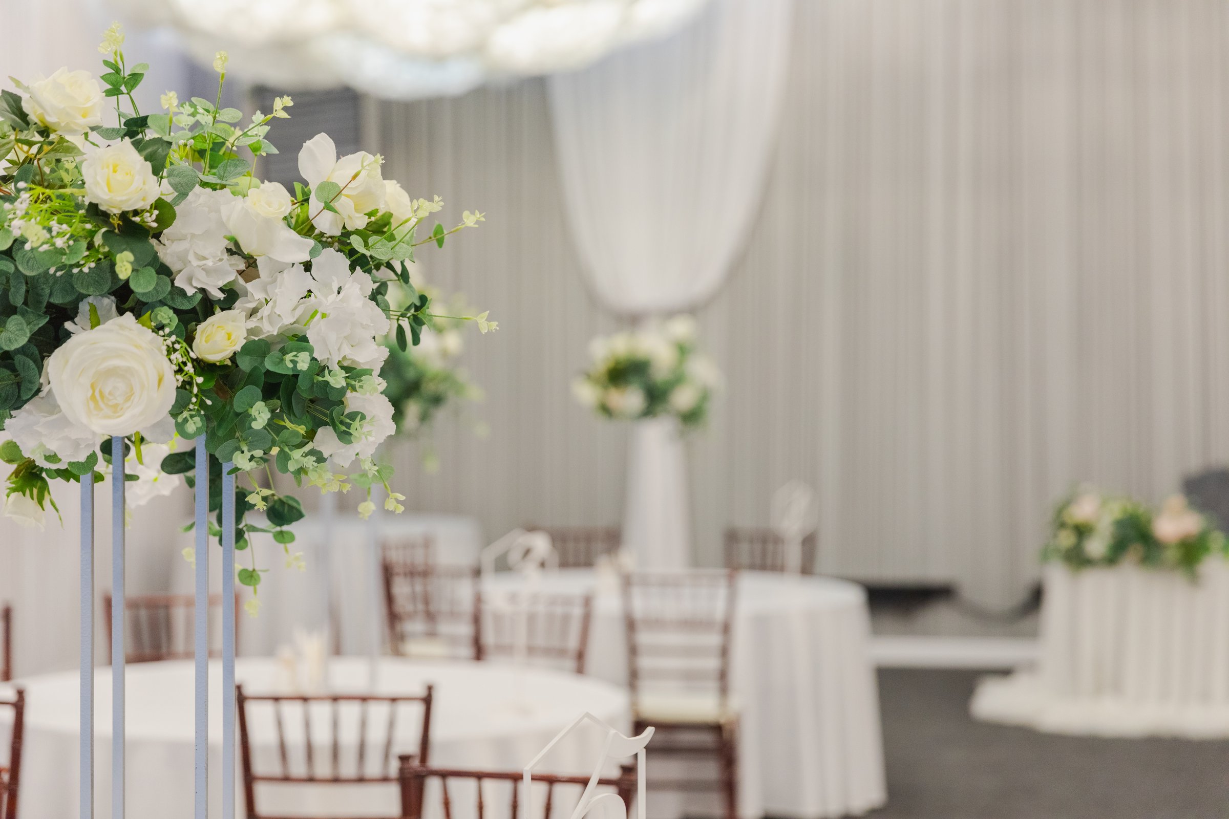 Decorated interior for festive event. Fancy table set for dinner with white flower composition in restaurant, luxury interior background. Wedding elegant banquet decoration arranged by catering service