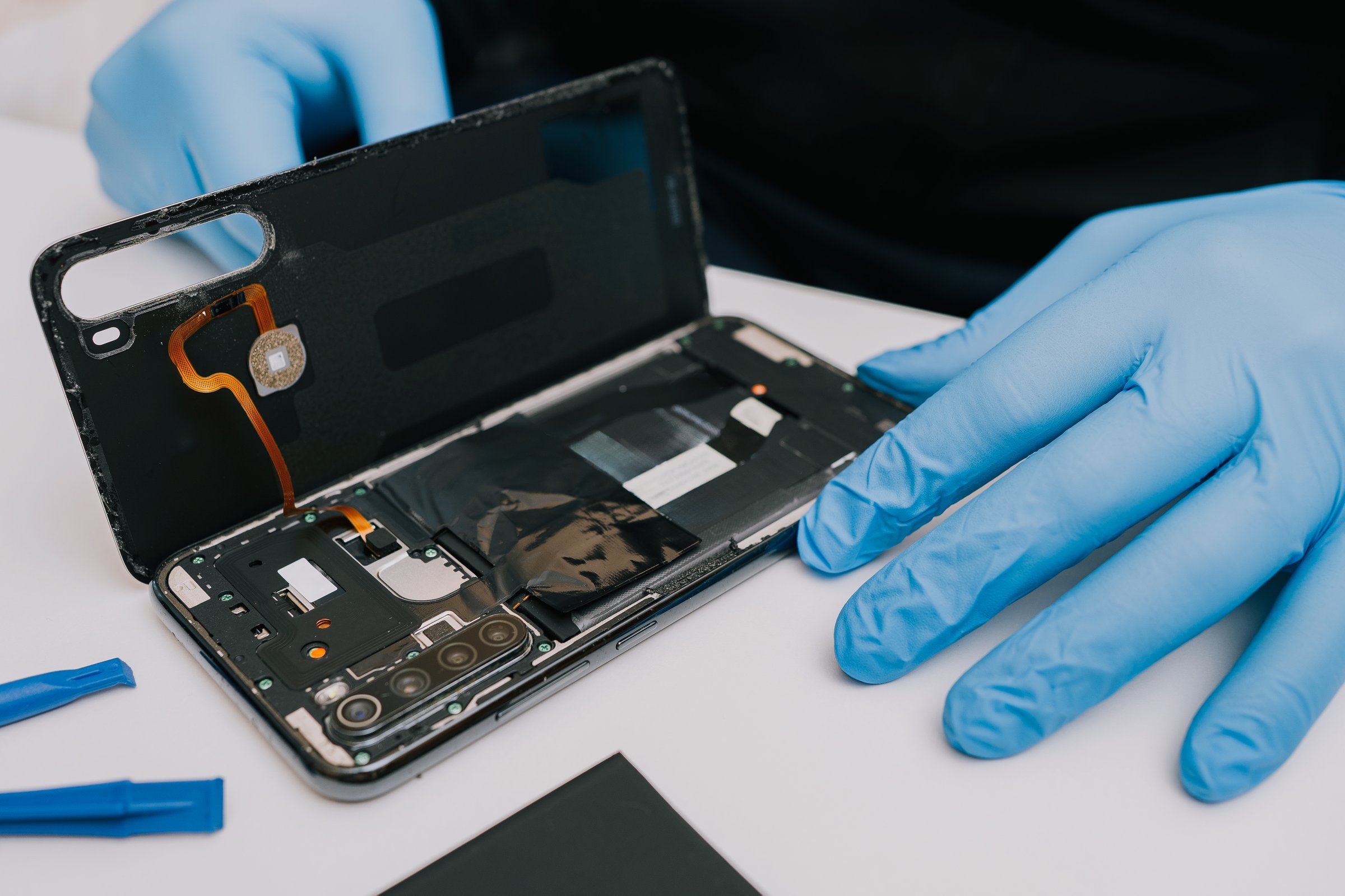 Battery replacement in a mobile phone â a technician in protective gloves disassembles a smartphone, removing the back cover to install a new battery. Repair and maintenance process of electronics.