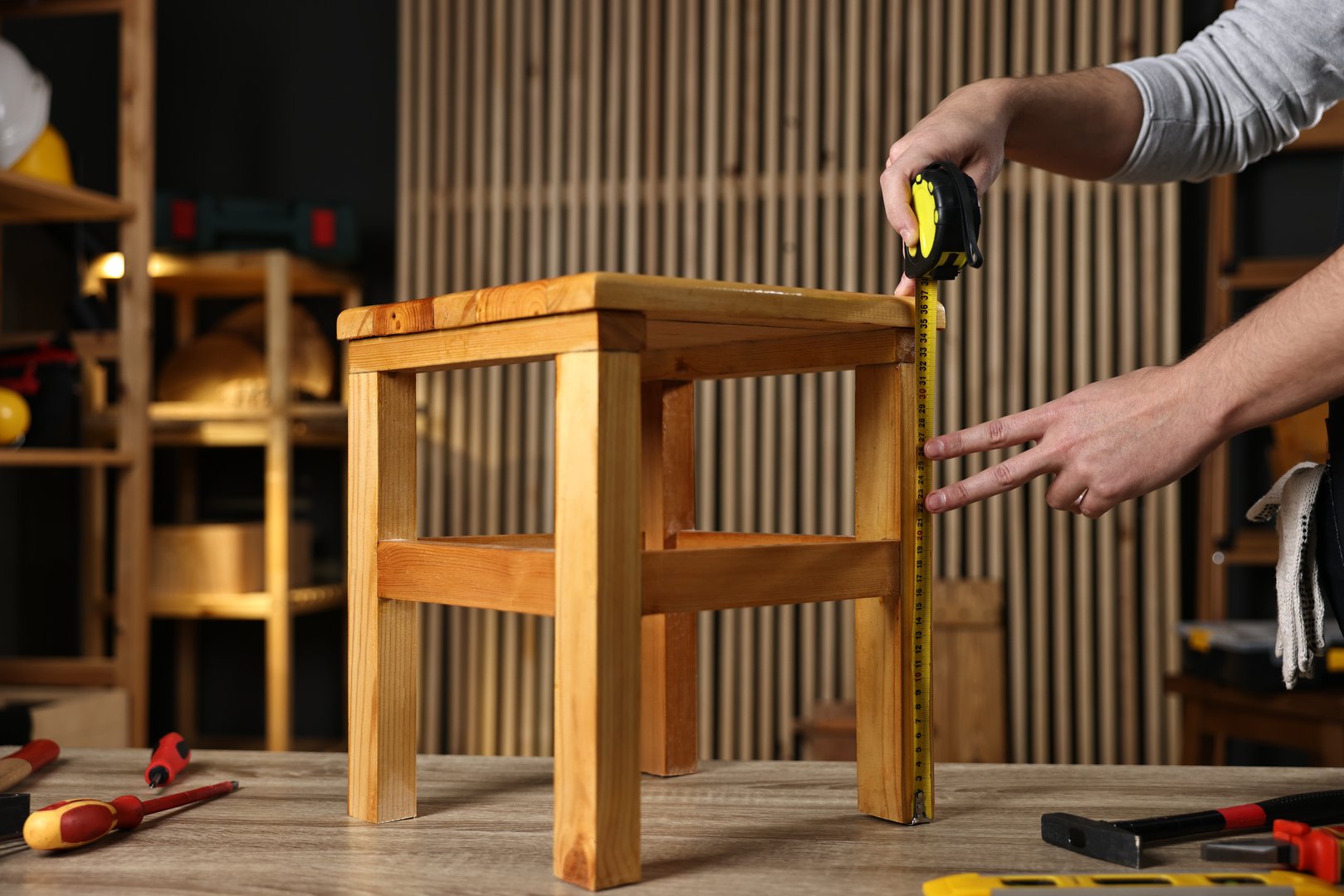 Repairman measuring wooden stool at table in workshop, closeup
