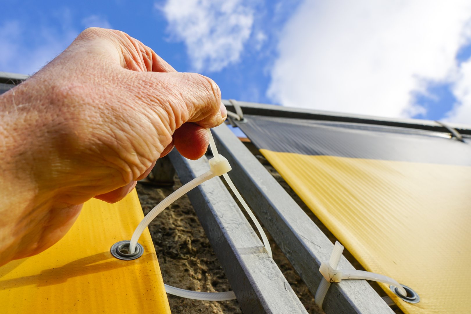 Fastening process of the outdoor vinyl advertising banner to the metal frame with the help of plastic cable ties, billboard fastening to frame