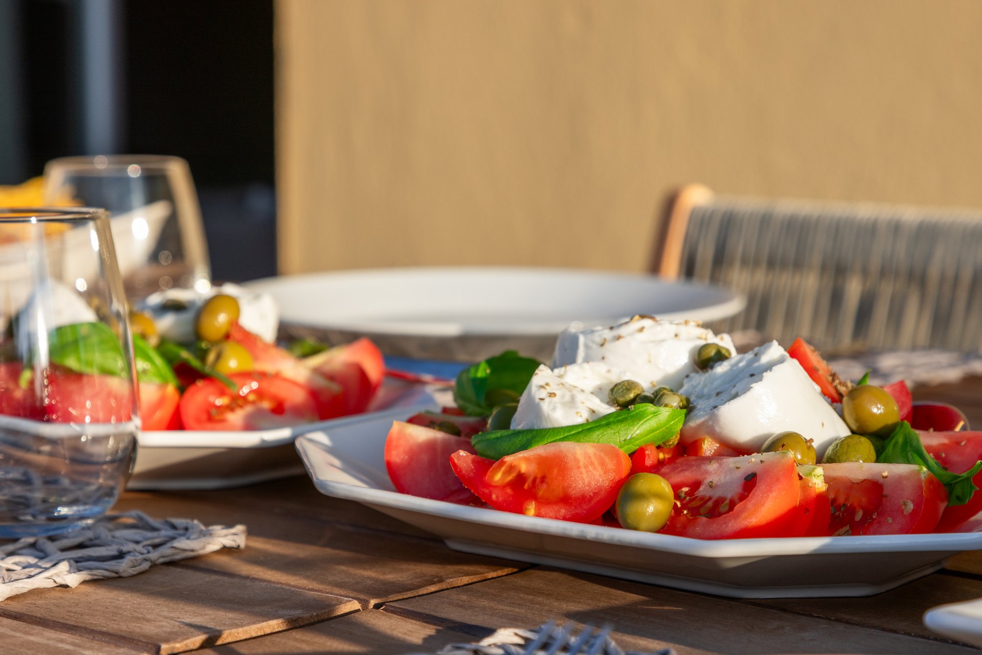 A sun kissed table presents a classic Caprese salad, with Mozzarella cheese, juicy tomatoes, green olives, and a sprinkle of capers, epitomizing Italian summer lunch